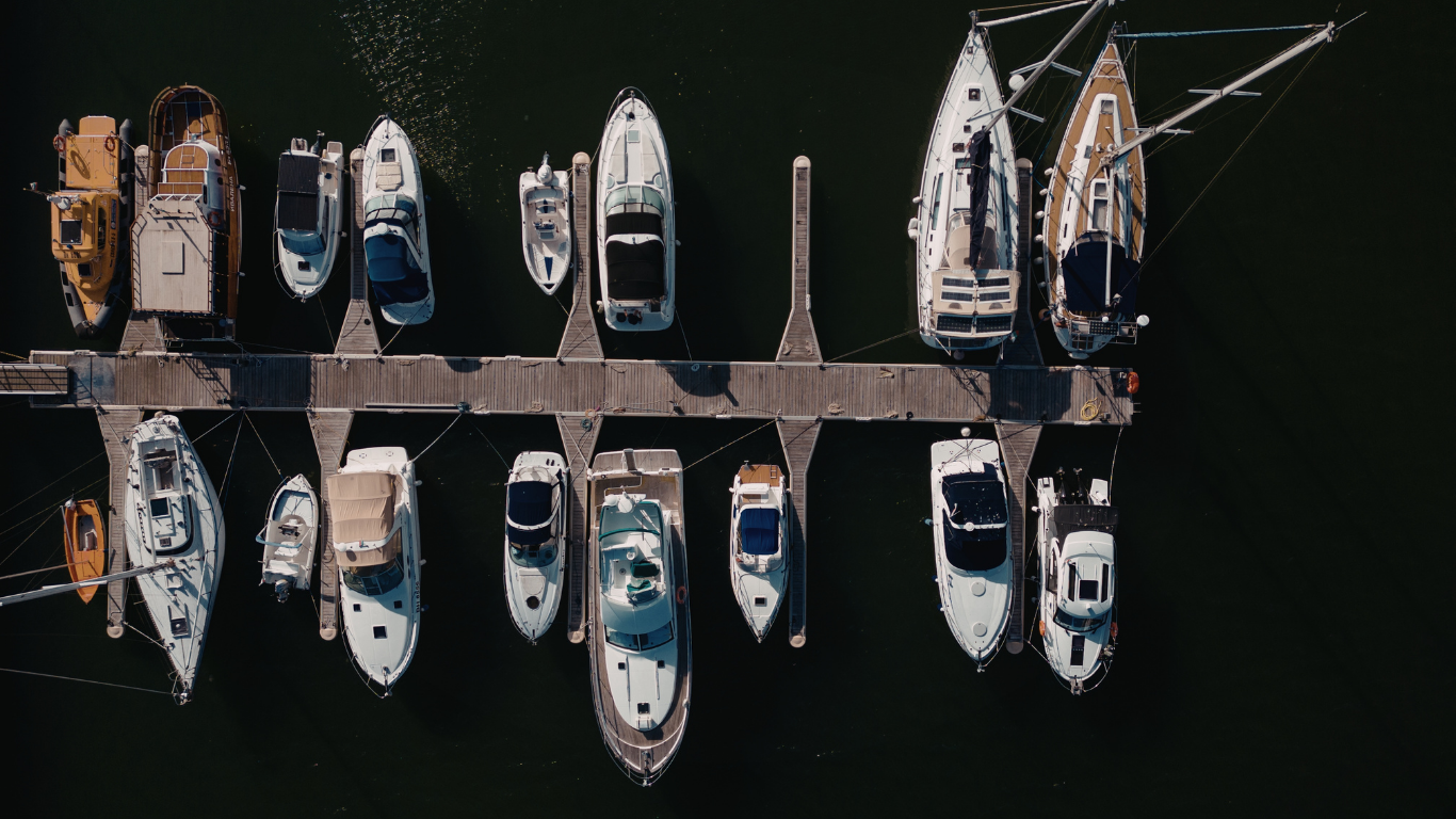 Overhead view of several docked boats along a pier in dark water at a marina