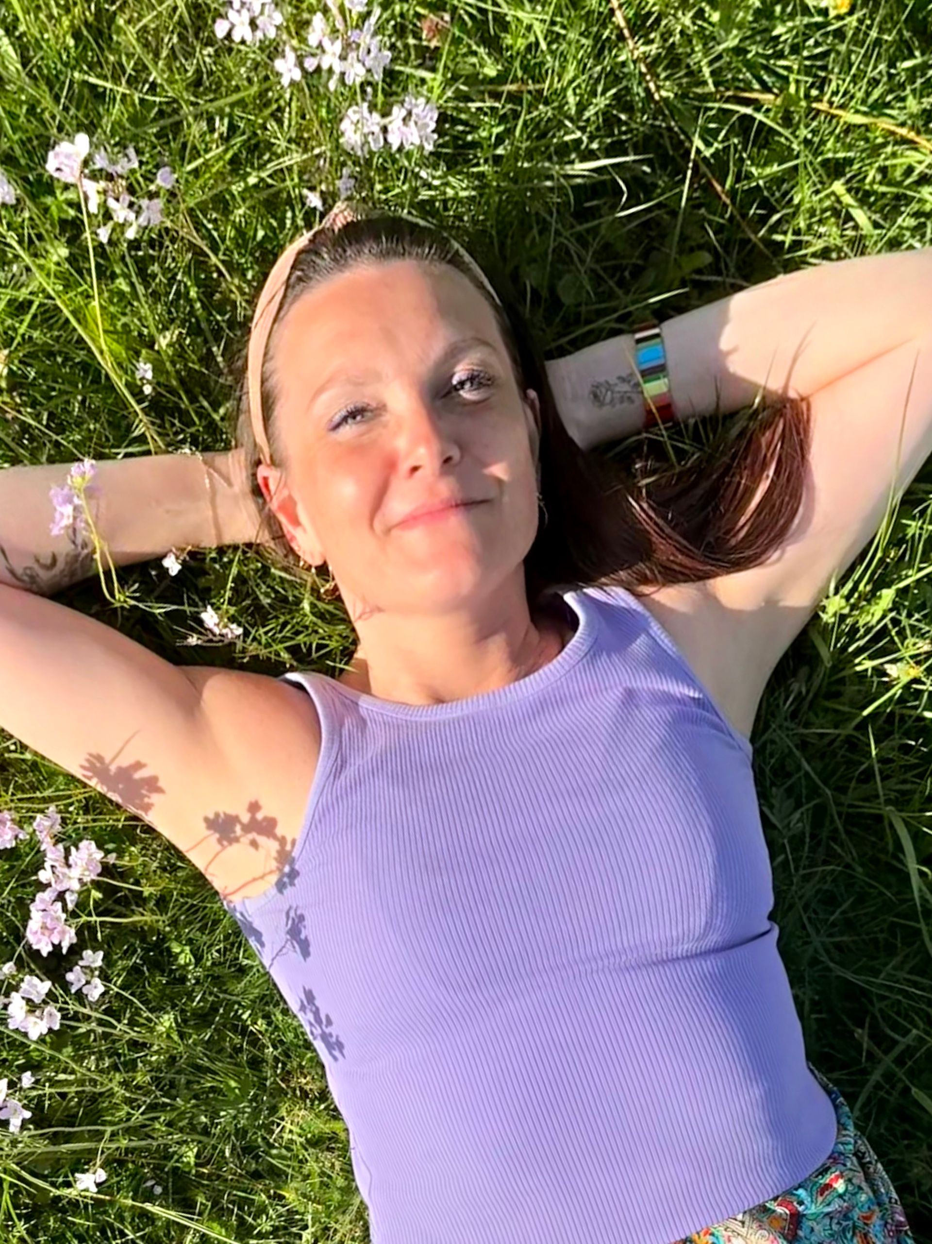 Sabine FHealS met een witte top en een ketting met een stenen hanger, tegenlicht van de felle zon in een veld bij zonsondergang.