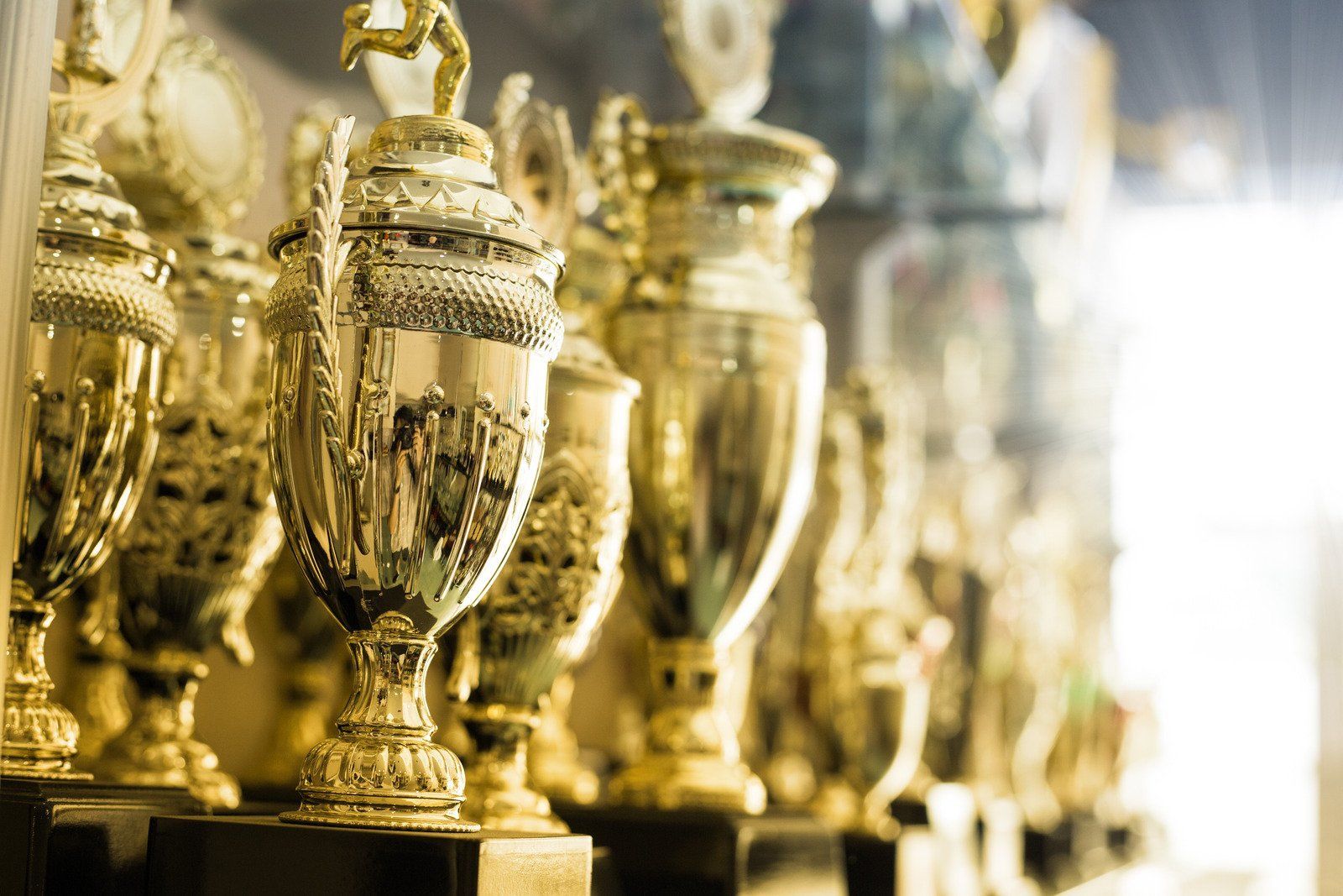 Golden trophies on a shelf; celebration or recognition, displayed in a row, with a bright light source.