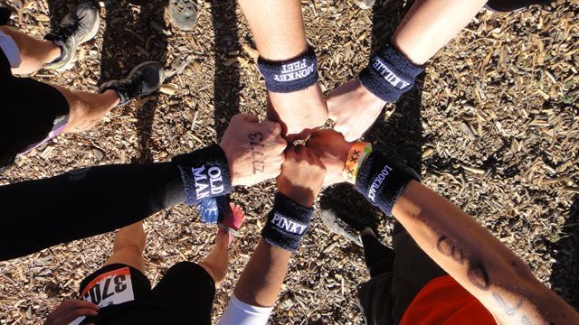 Hands in a circle, fists touching, wearing sweatbands. Some wristbands say 