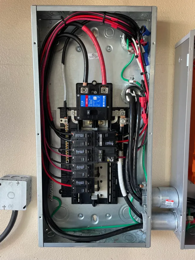 Open electrical panel with black and red wires, circuit breakers, and a digital display.