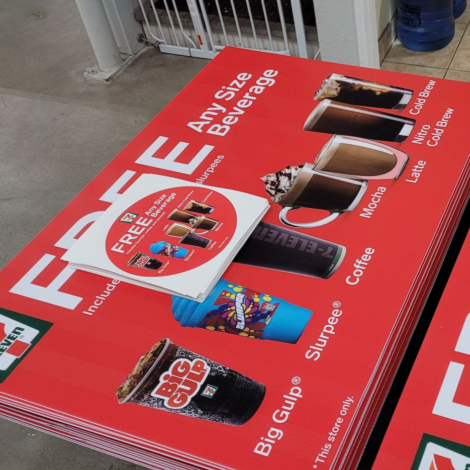 Red promotional floor sign for free beverages, with drink images and labels on a store floor
