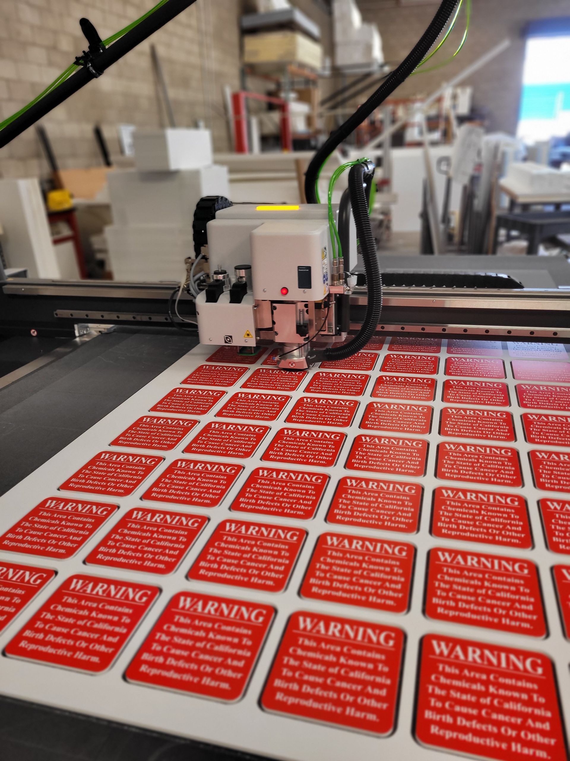 Industrial printer applying red warning labels on a sheet in a workshop