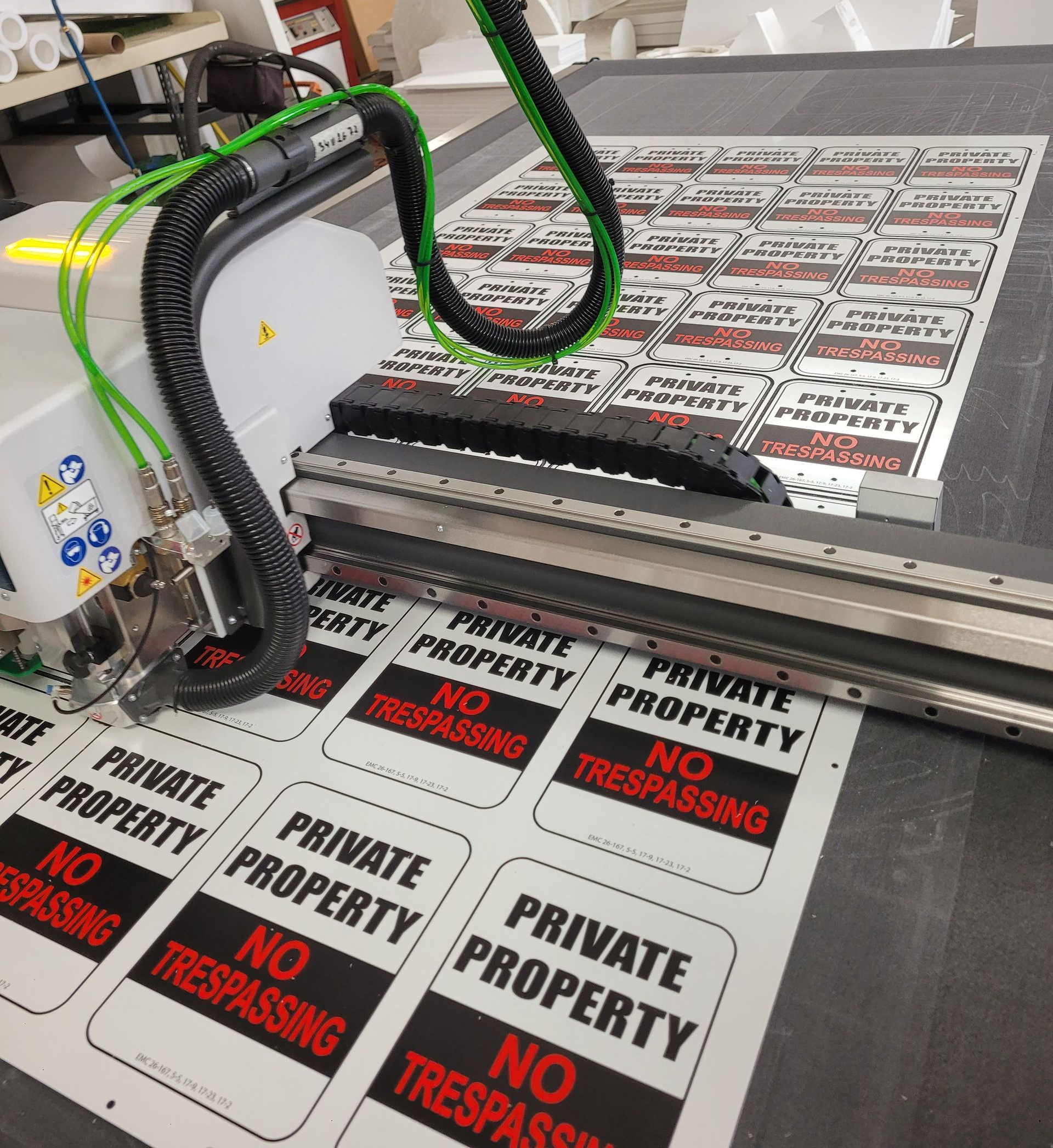 CNC router engraving repeated “PRIVATE PROPERTY NO TRESPASSING” signs on a gray work surface