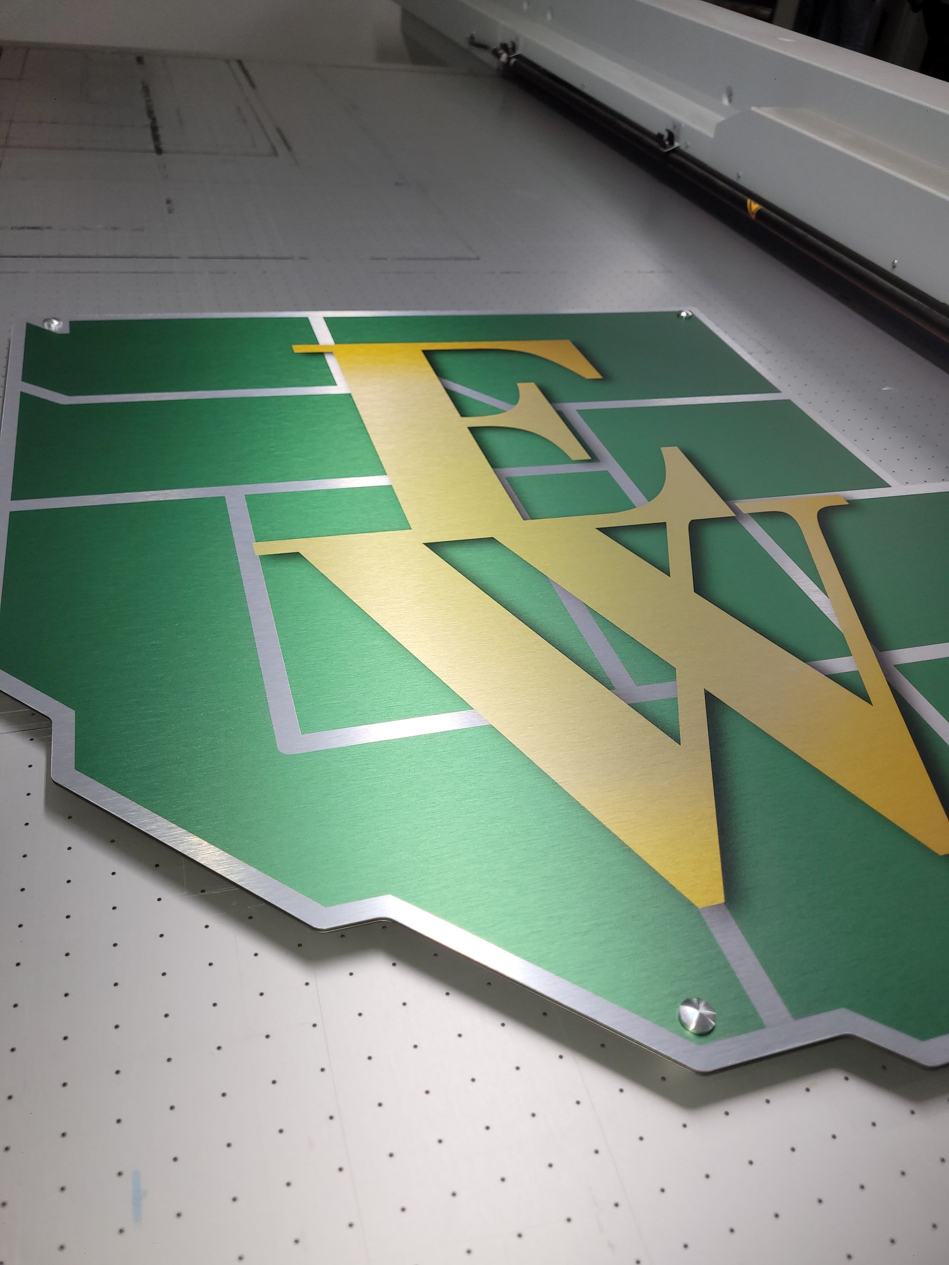 Green and gold WV logo on a wall-mounted sign with a silver border and diamond plate background