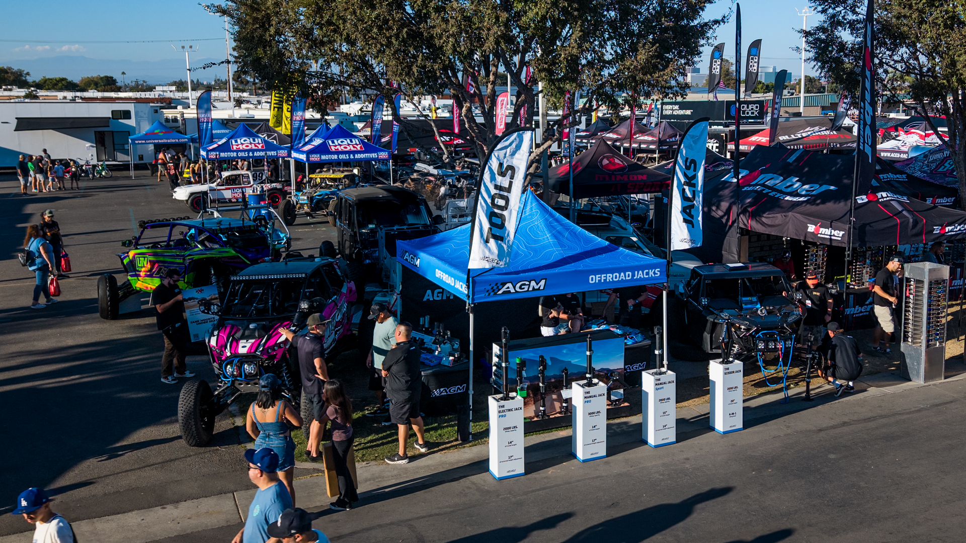 Outdoor motorcycle rally with blue tents, flags, and parked bikes in a sunny lot