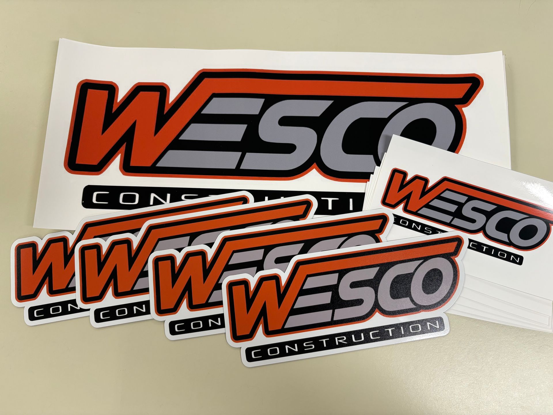 Stack of WESCO Construction logo stickers in orange, black, and gray on a light background