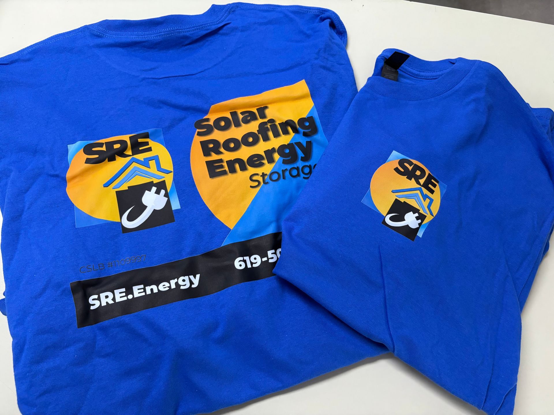 Blue Solar Roofing Energy t-shirts with yellow logo laid out on a white surface