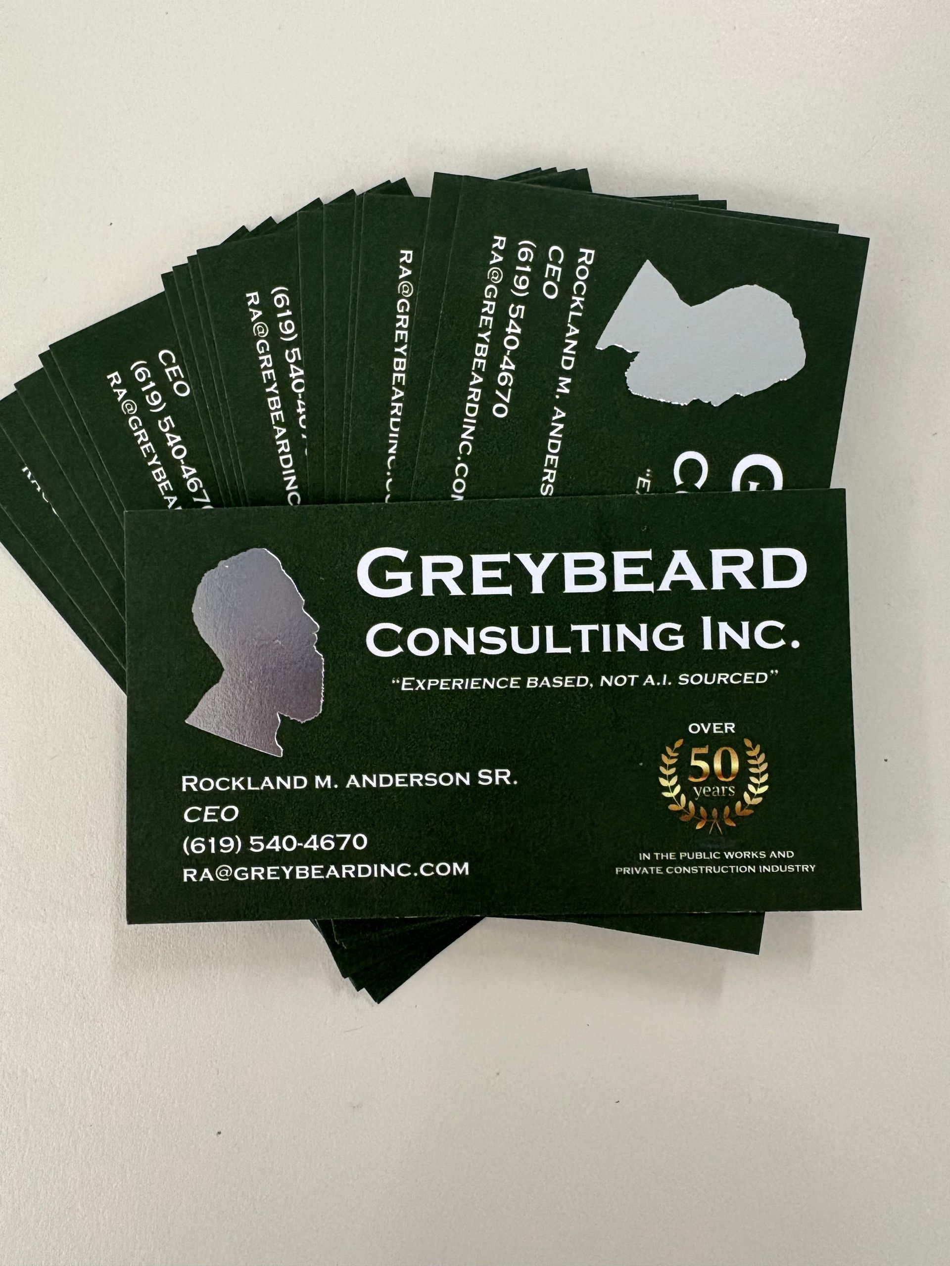 Stack of dark green Greybeard Consulting Inc. business cards with white text on a light surface