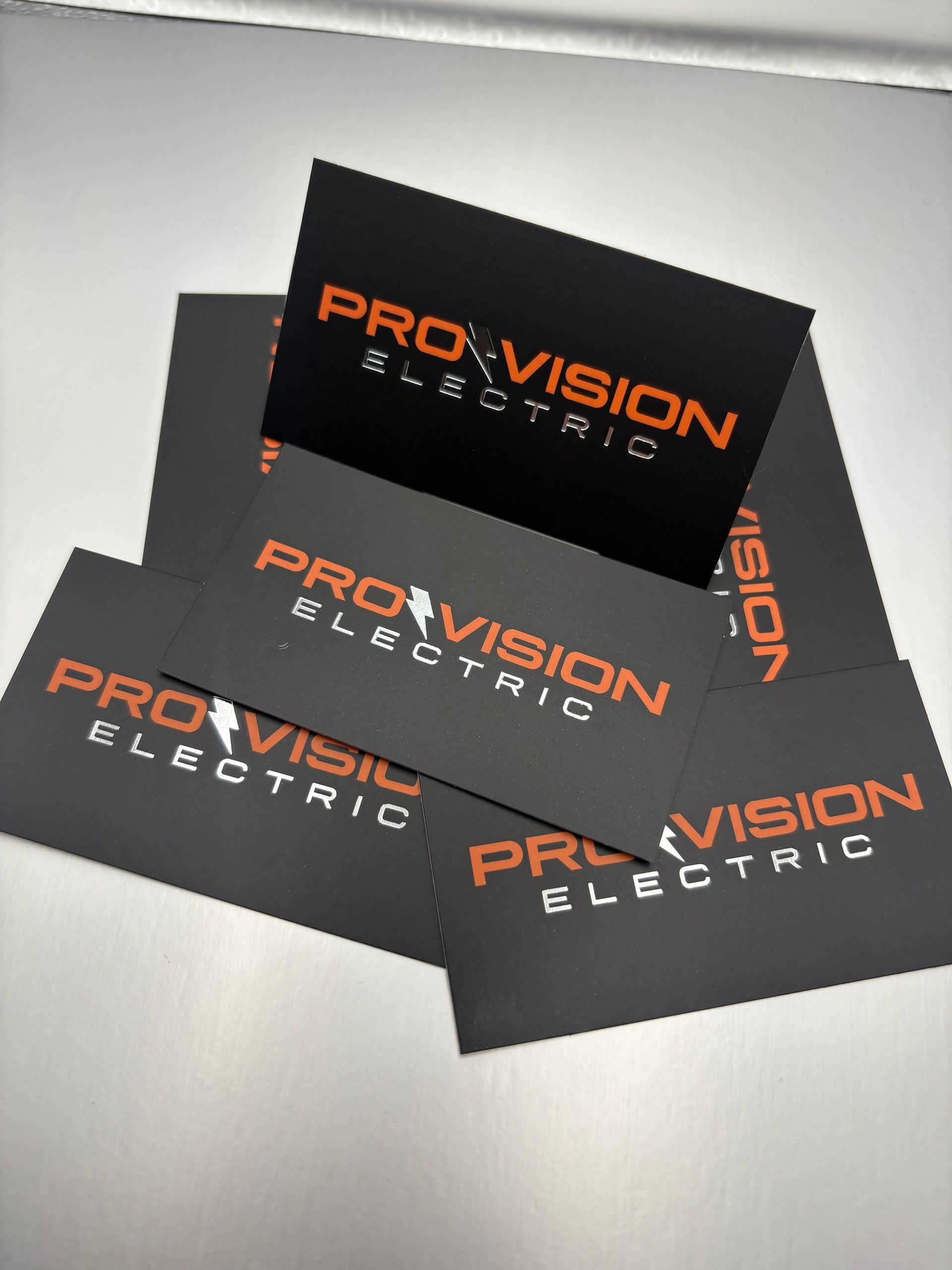 Promotional business cards for PRO-VISION Electric in black and orange, fanned out on a light surface