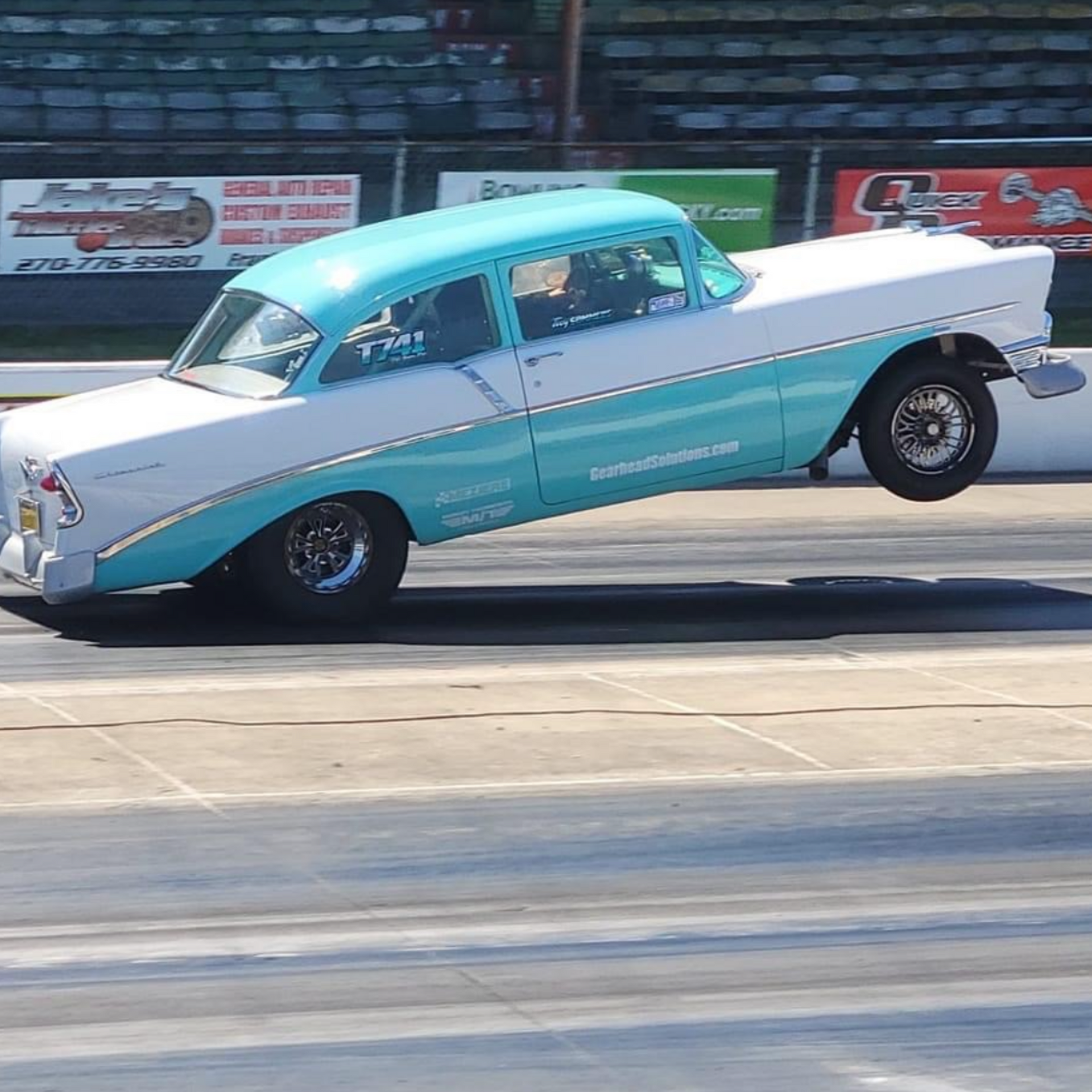 Light blue and white classic car lifting its front wheels during a drag race on a track