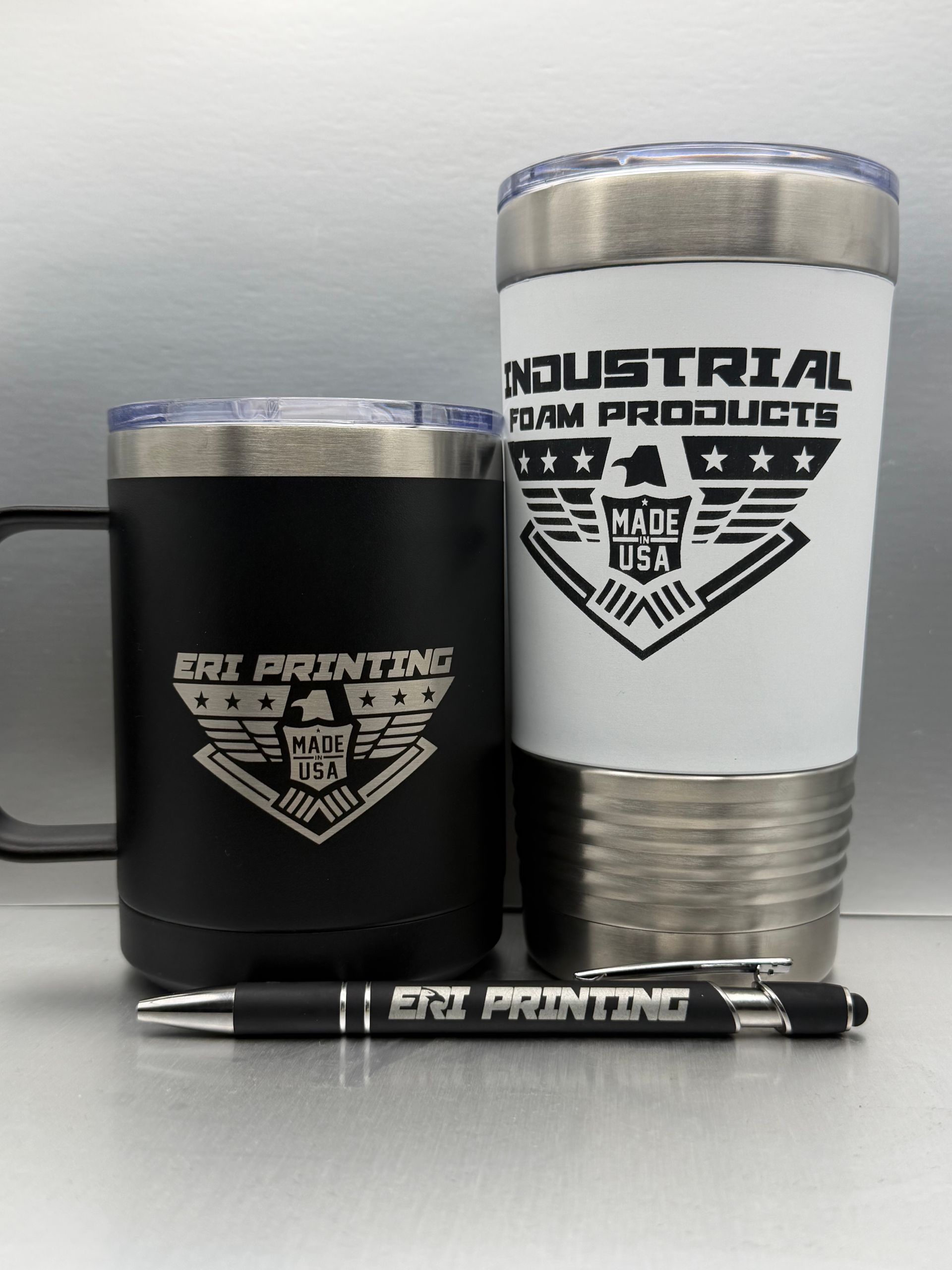 Black and white branded tumblers with a matching pen on a tabletop