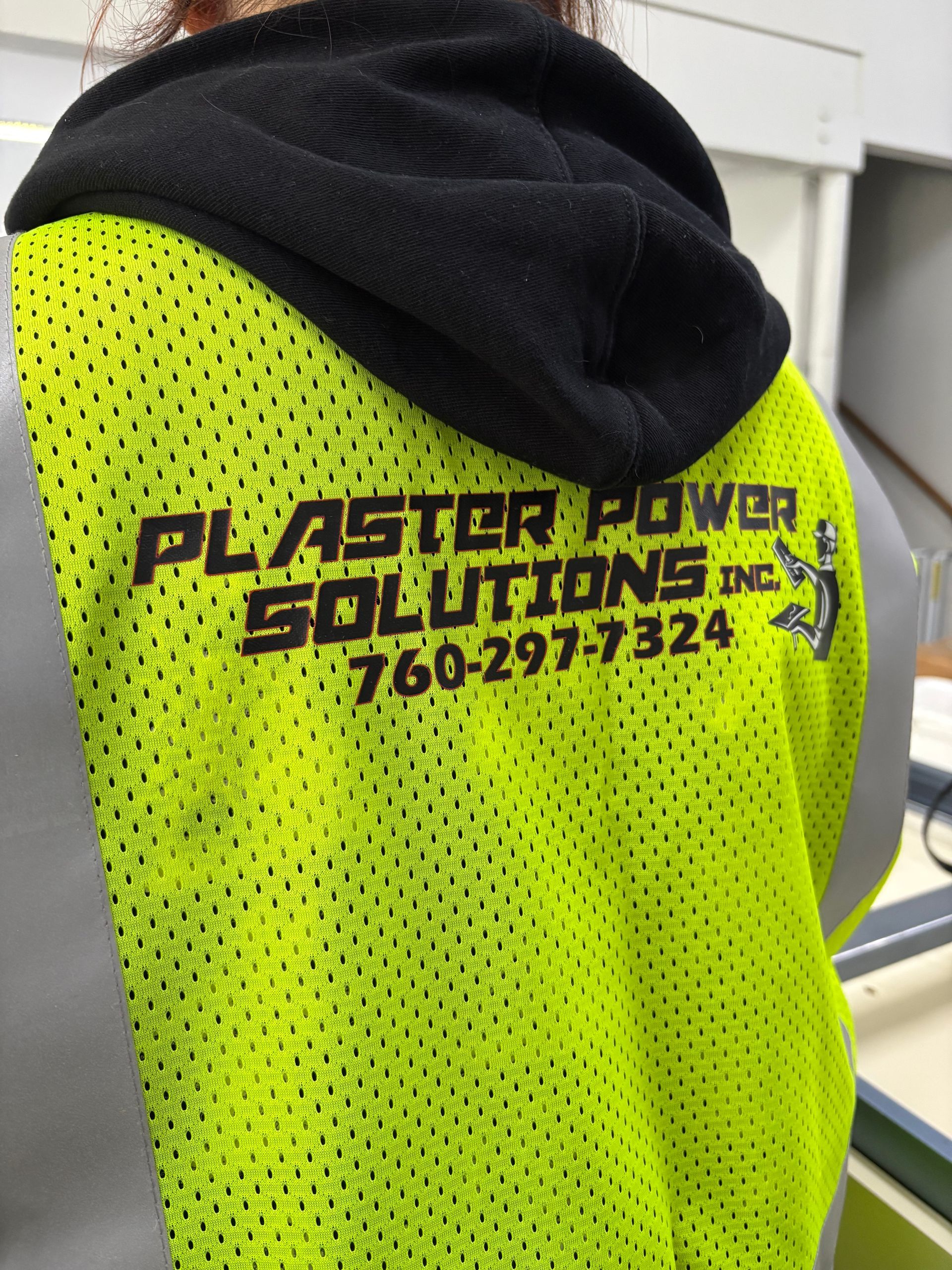 Person wearing a neon yellow work shirt with black logo text and a dark hooded layer.