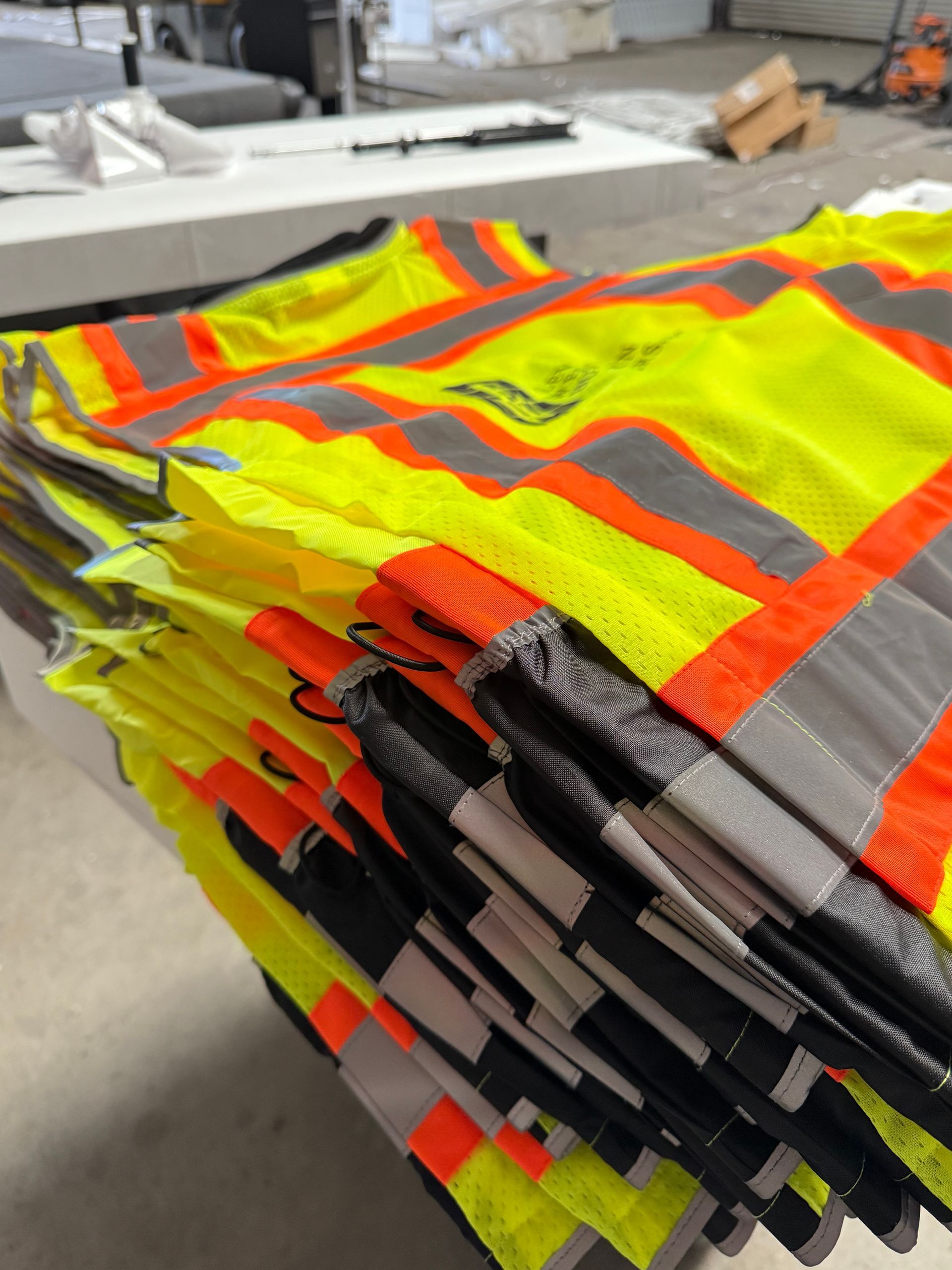 Stacked neon yellow and orange safety vests on a table in an outdoor work area
