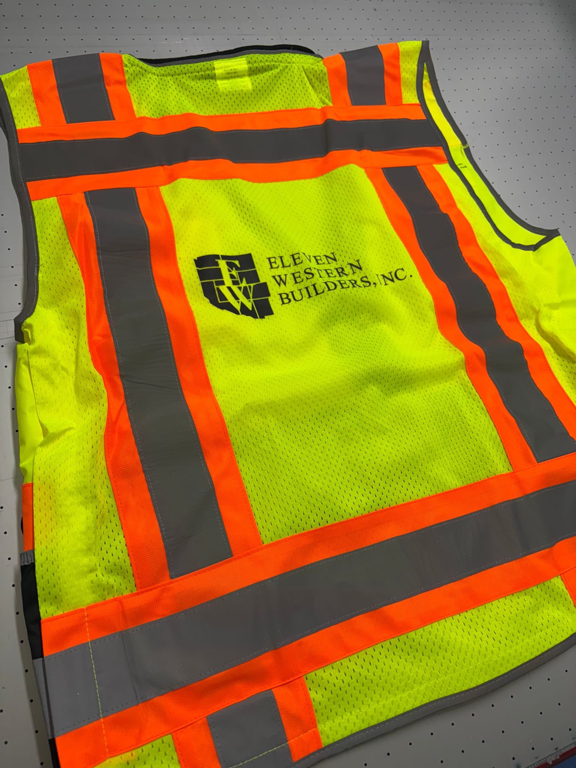High-visibility neon yellow safety vest with orange reflective stripes on a gray floor