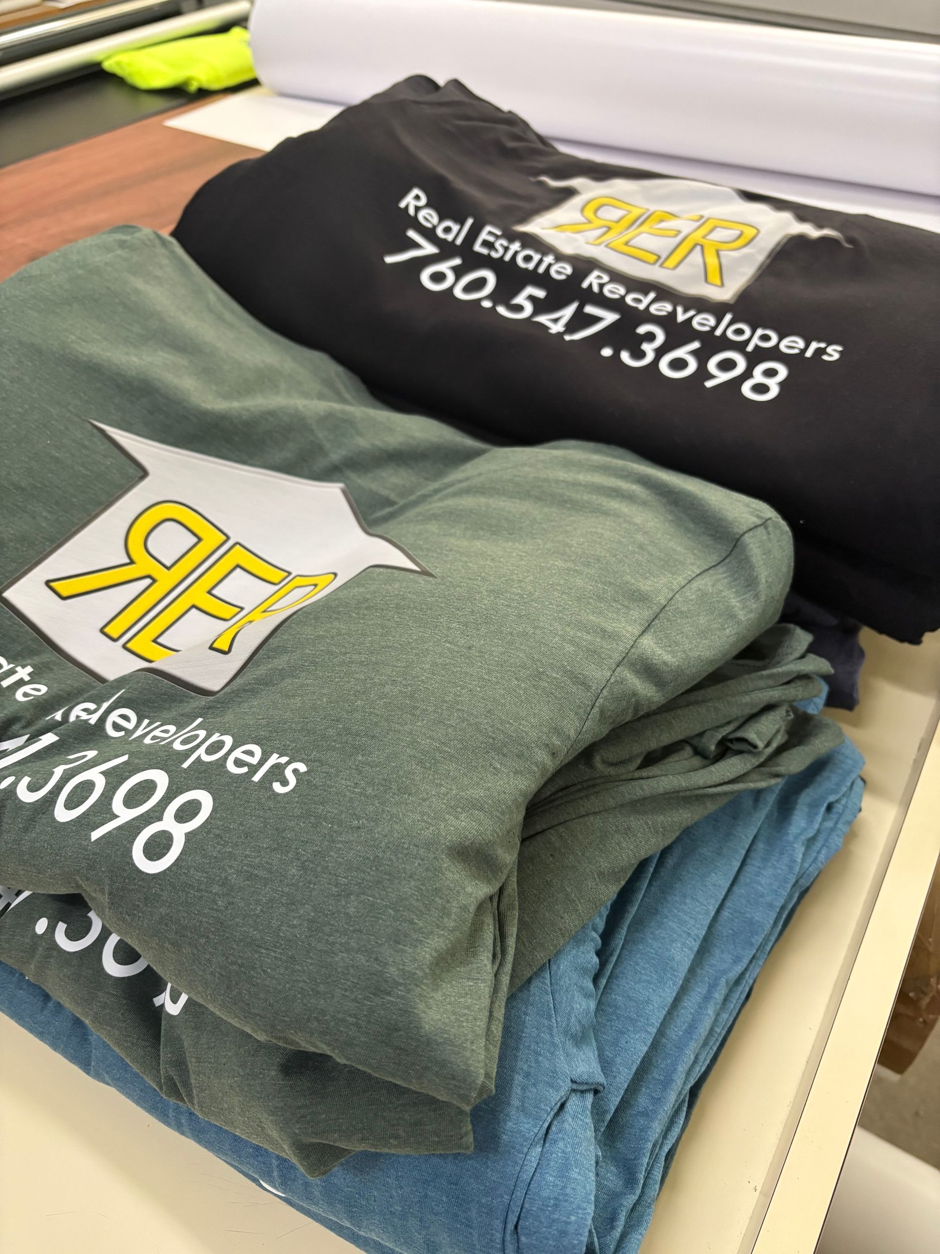 Stacked folded sweatshirts with a “BP” logo and phone number in a store or workspace.