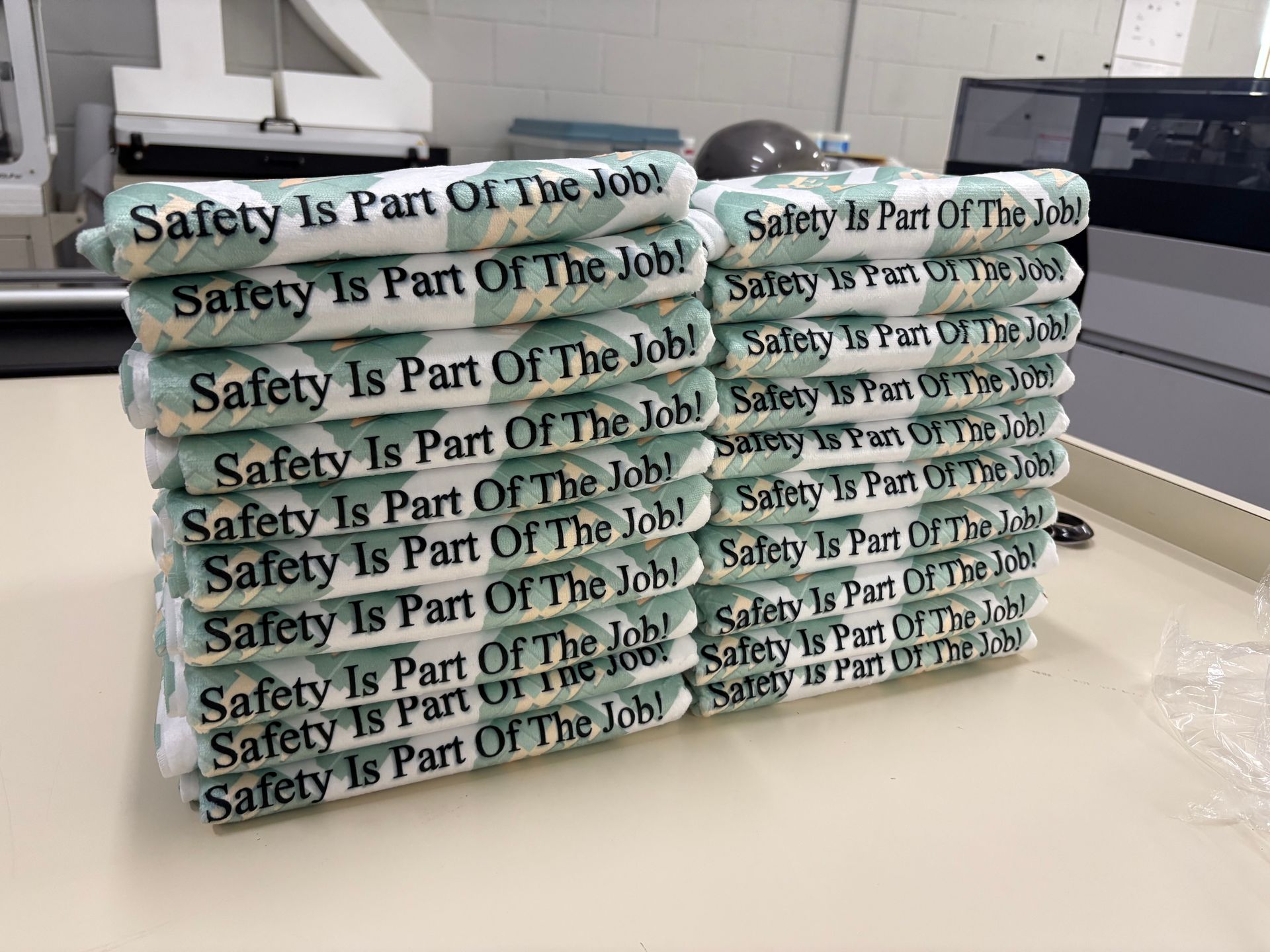 Stack of mint-green face masks printed with “Safety Is Part Of The Job” on a table in a bright room