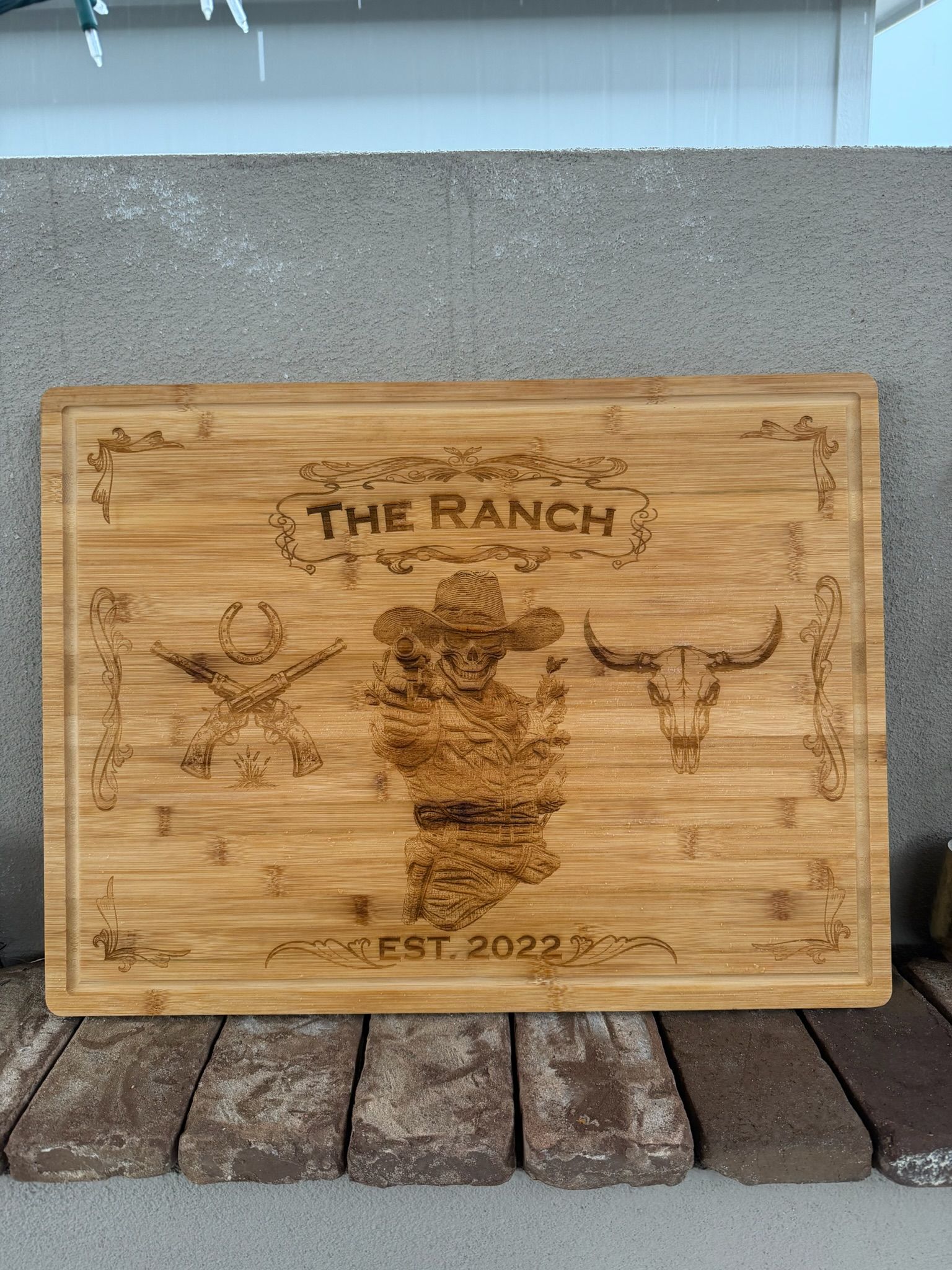 Wooden sign engraved “THE RANCH” with a longhorn skull and rustic western motifs, leaning against a wall.