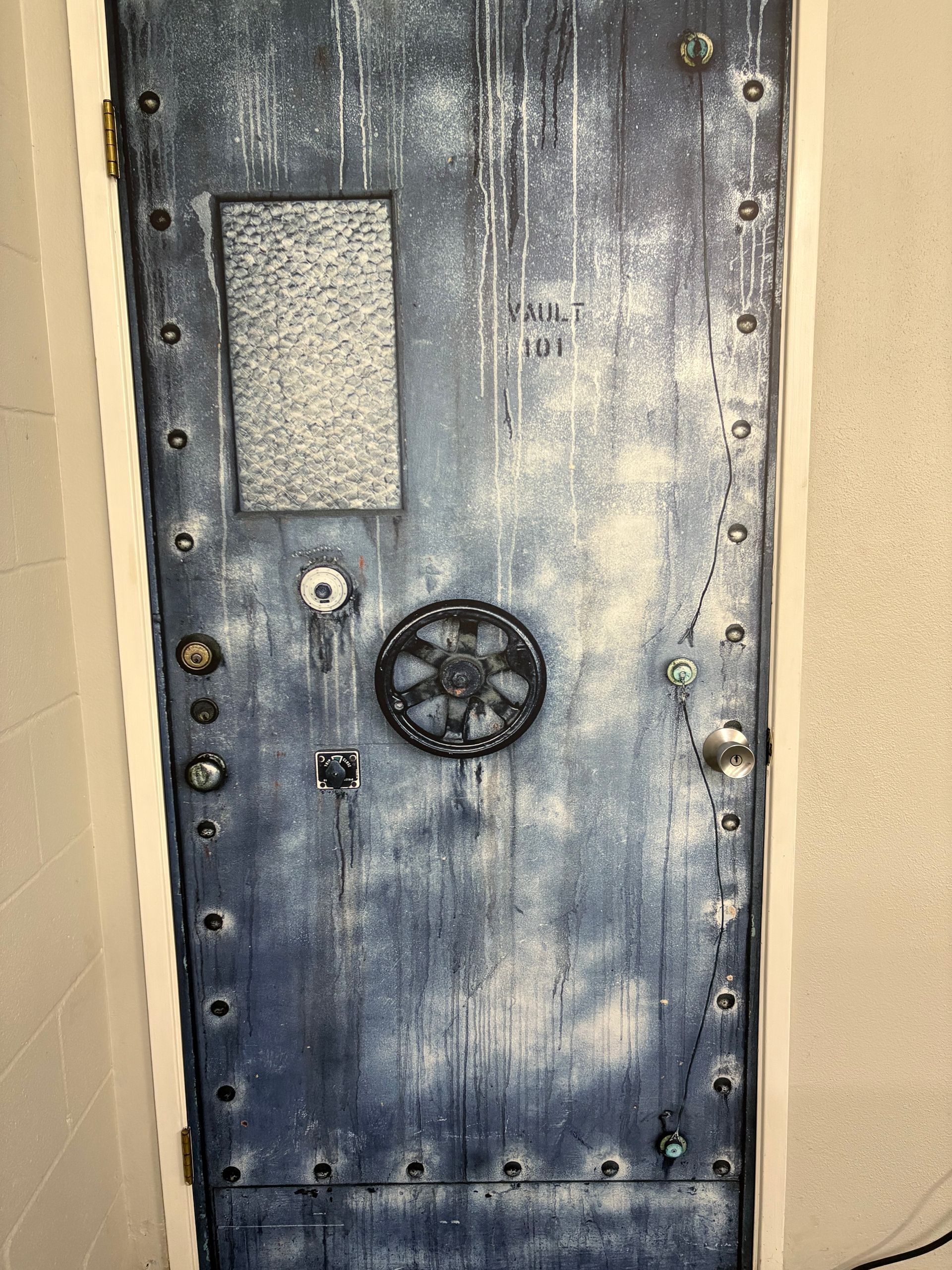 Old gray metal vault door wallpaper with a small window and large circular wheel handle in a wall opening