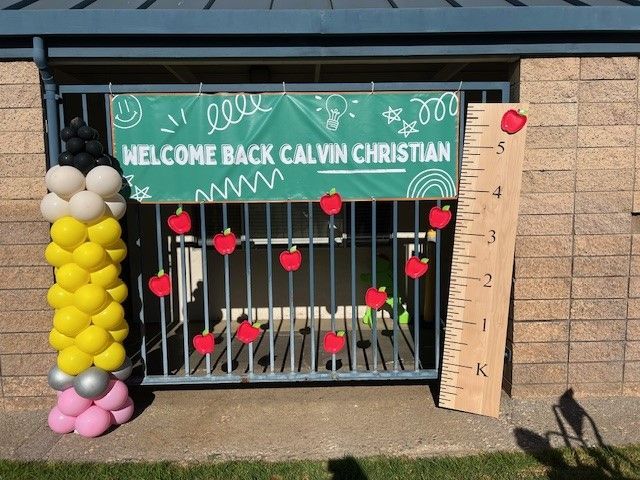 Welcome back Calvin Christian sign with balloon decorations and a growth chart by a window
