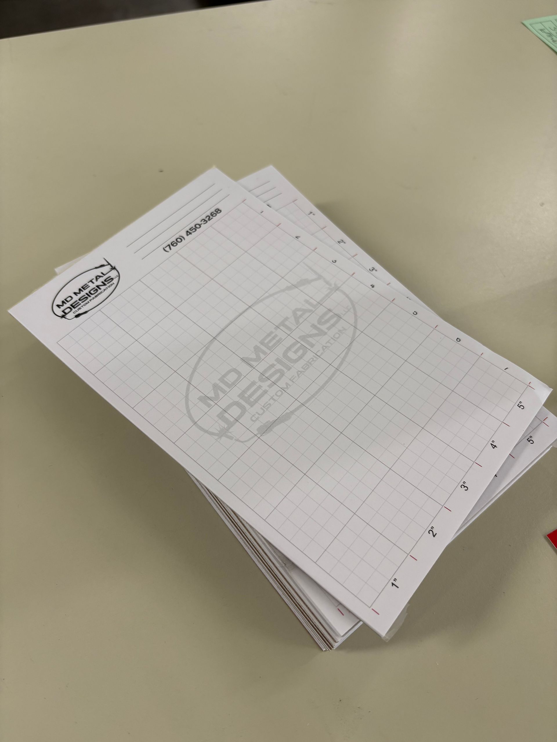 Stack of white grid paper sheets with handwritten notes on a beige desk.