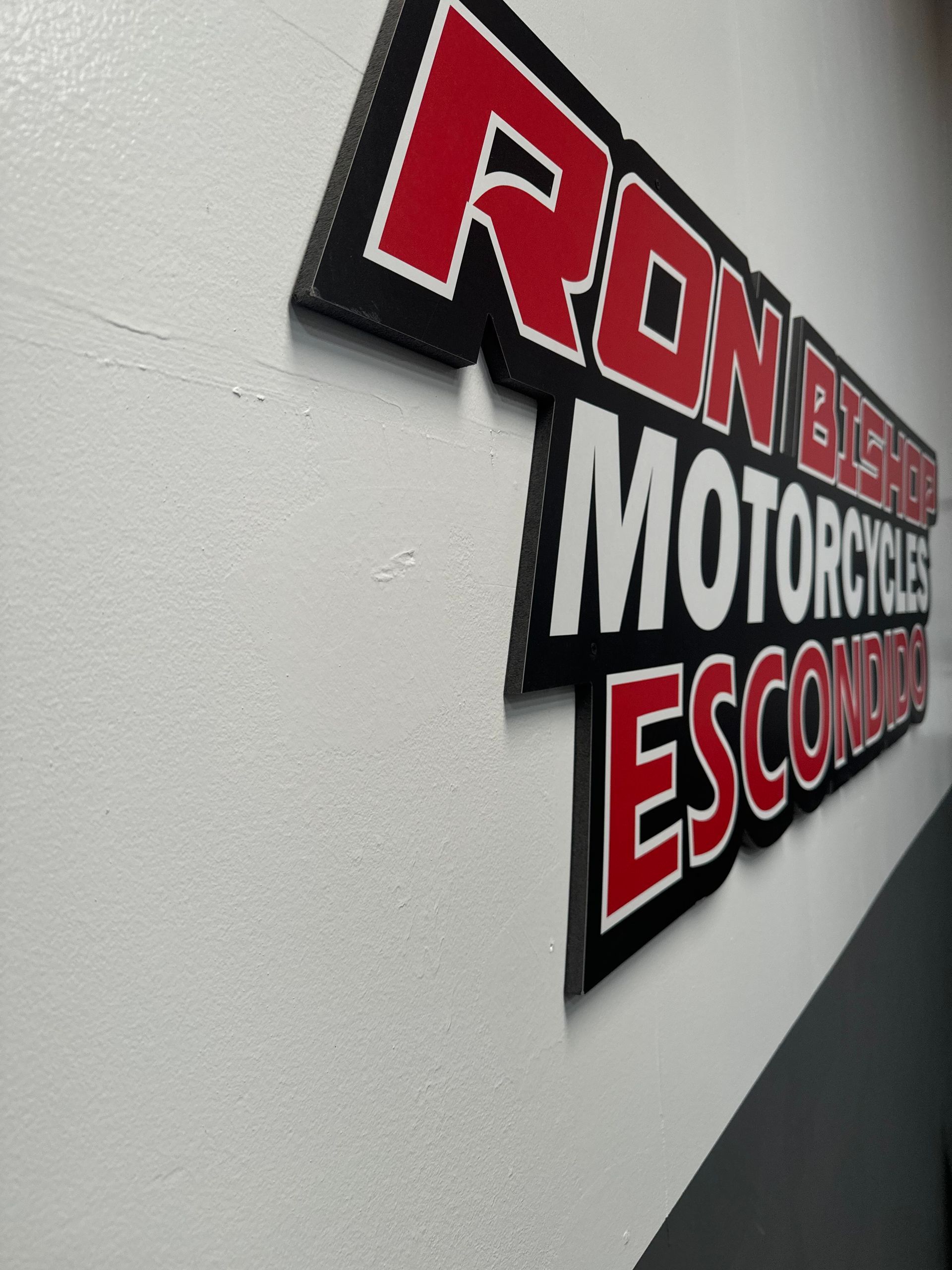 Wall sign reading “Ron B… Motorcycle” with bold red and white lettering on a textured white wall