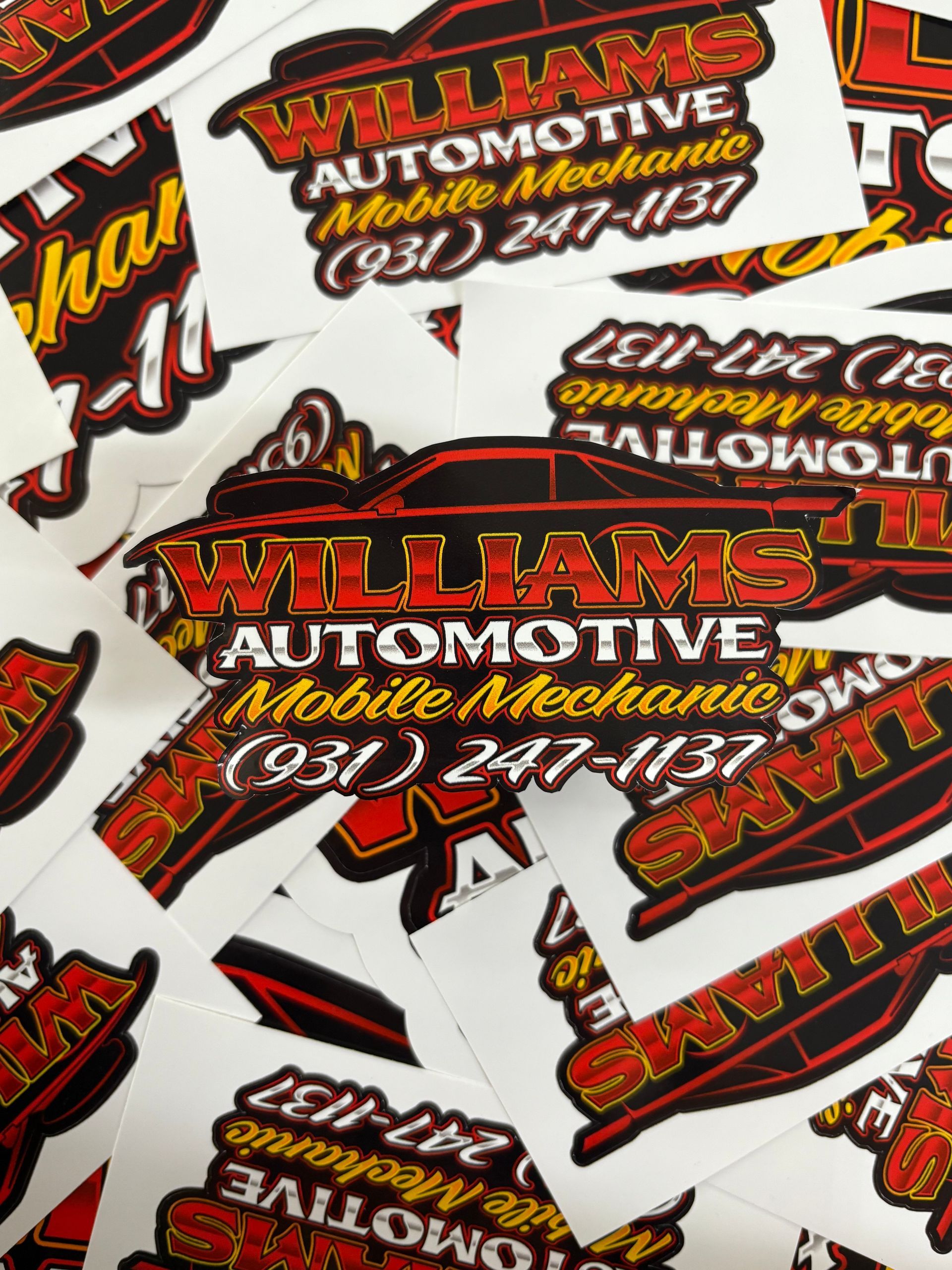 Stack of red, black, and white Williams Automotive Mobile Mechanic stickers with phone number and car logo