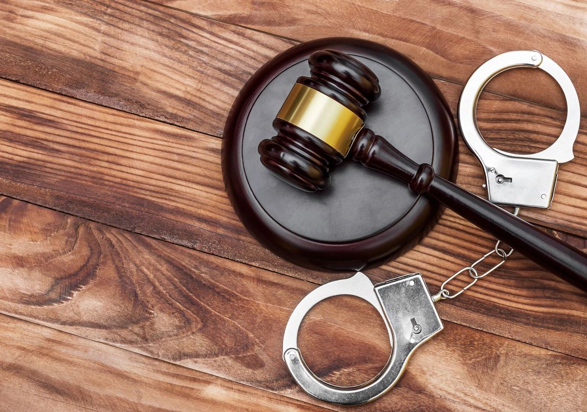 Gavel on a round base beside open handcuffs on a wooden table