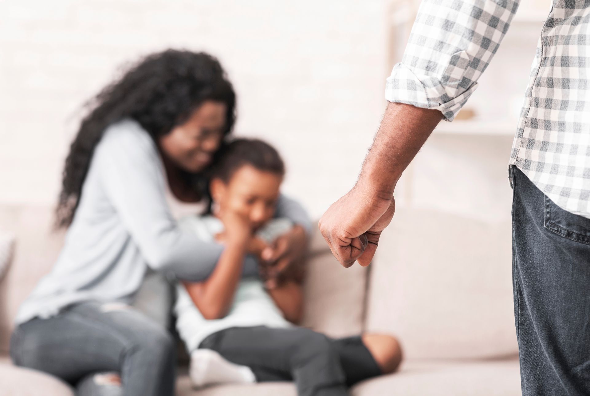 Person pointing toward a seated adult and child on a couch in a blurred living room