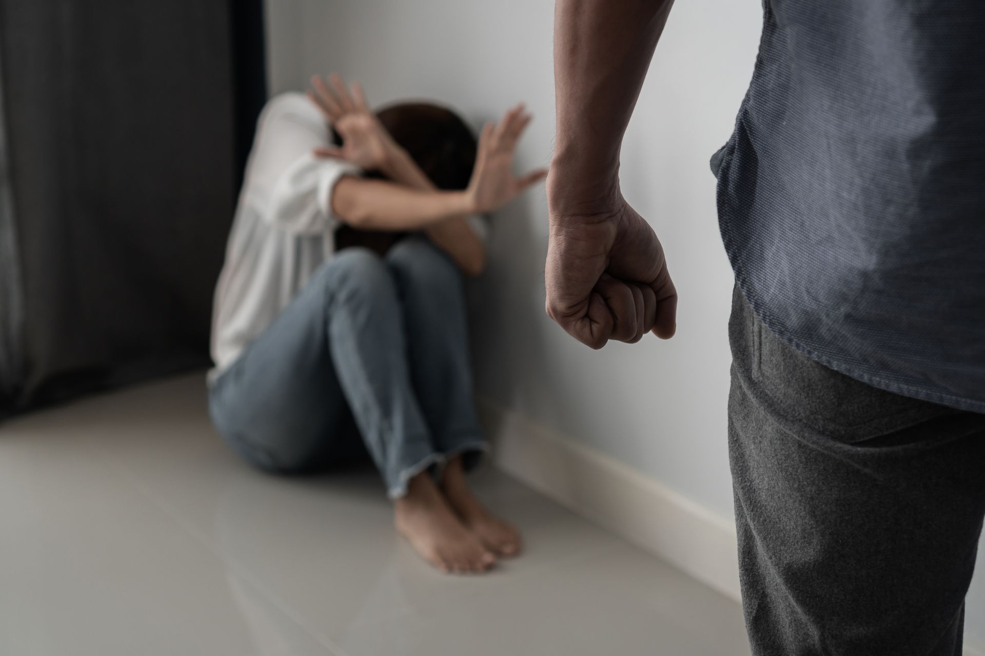 Person sitting on the floor against a wall while another person stands nearby, suggesting a tense confrontation