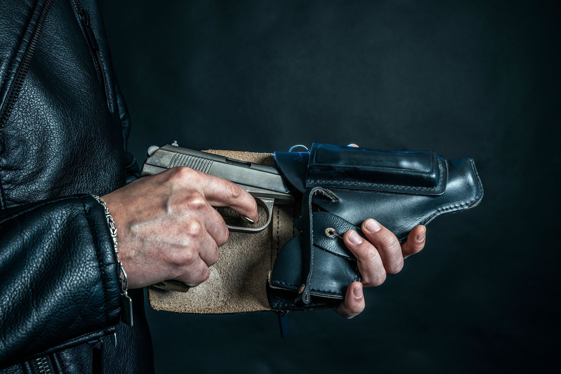 Close-up of a hand holding a handgun in a leather holster, with a second hand nearby.