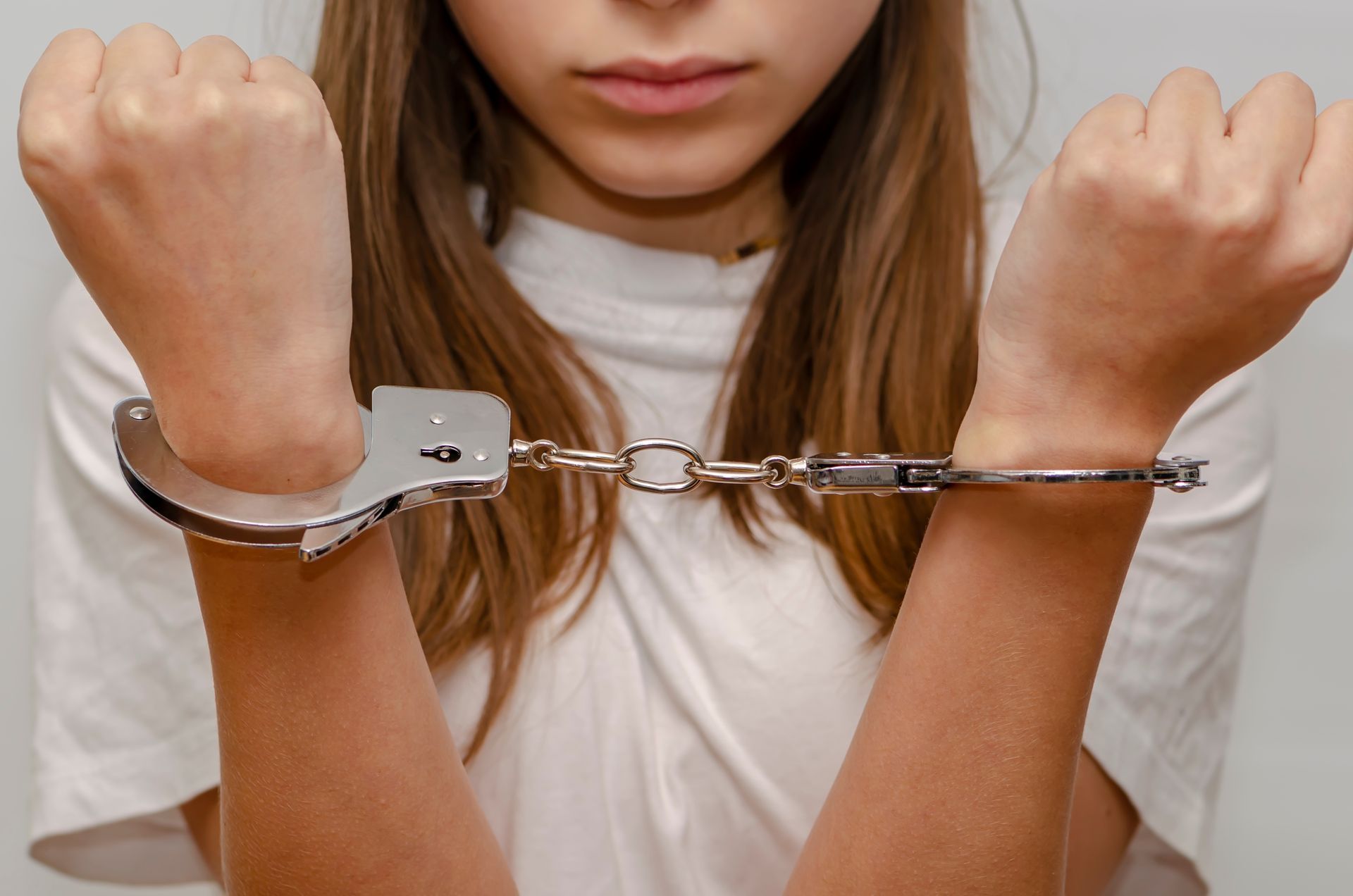 Person in handcuffs with arms raised, wearing a white shirt against a plain background