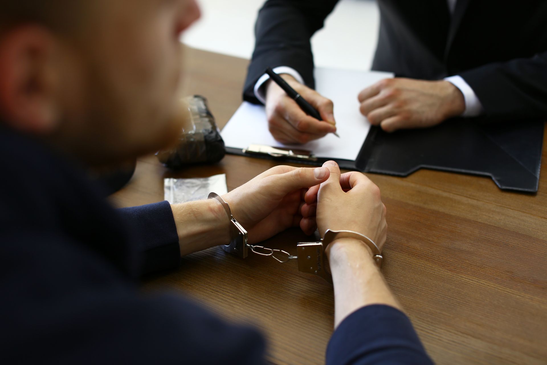 Two people in suits discussing a document at a wooden table, one writing with a pen.