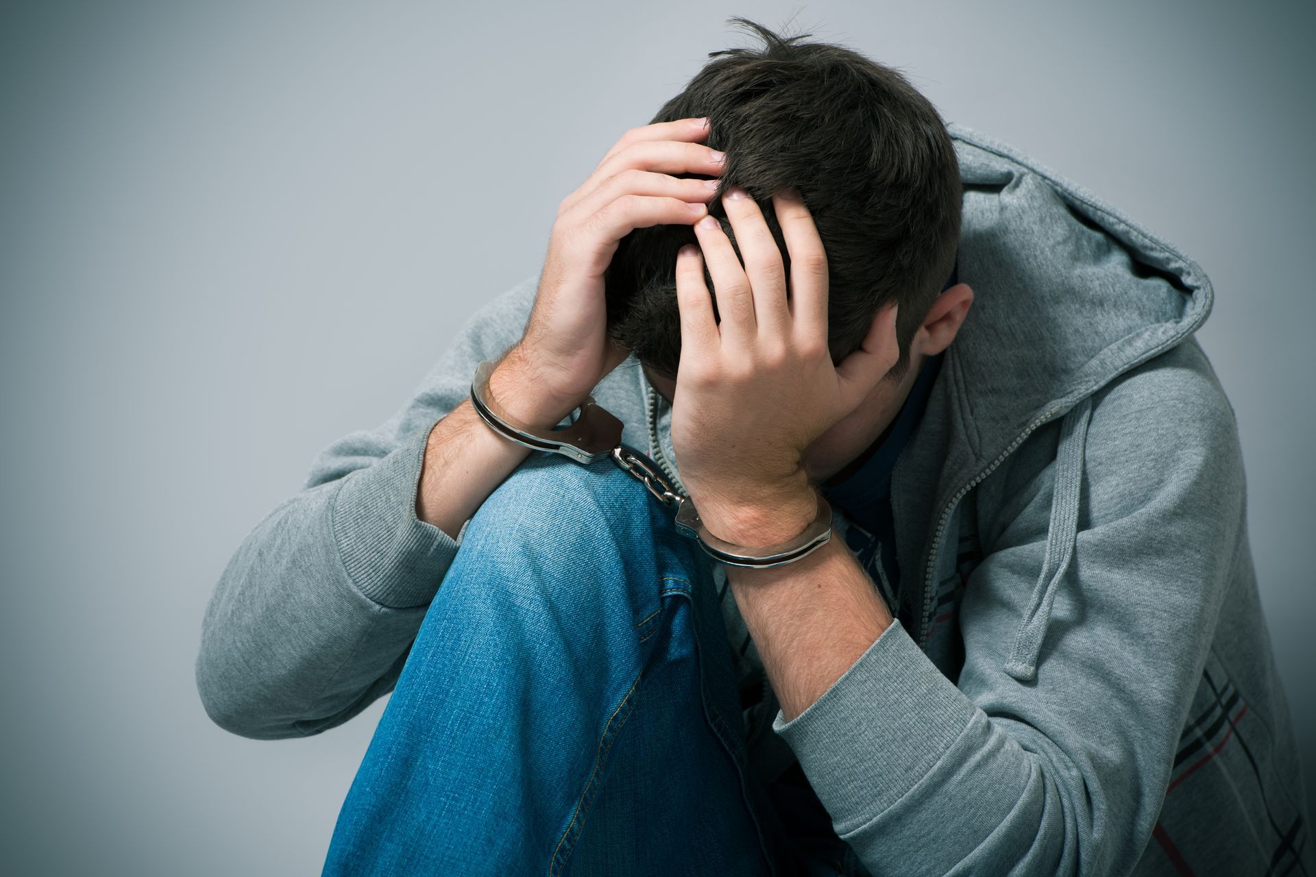 Person in a gray hoodie sits with head in hands, appearing distressed.