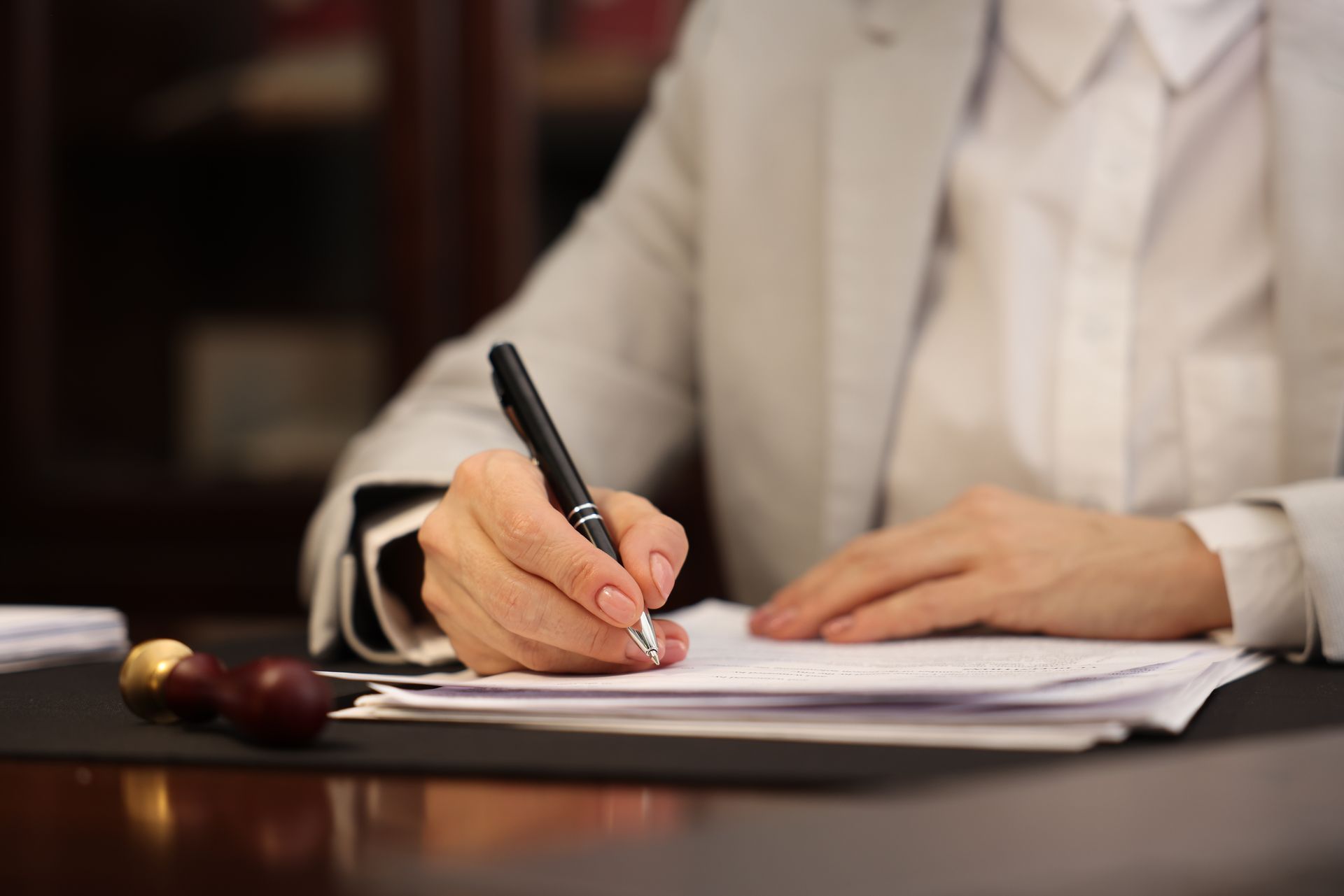 Person in a beige suit signing papers at a desk with a pen