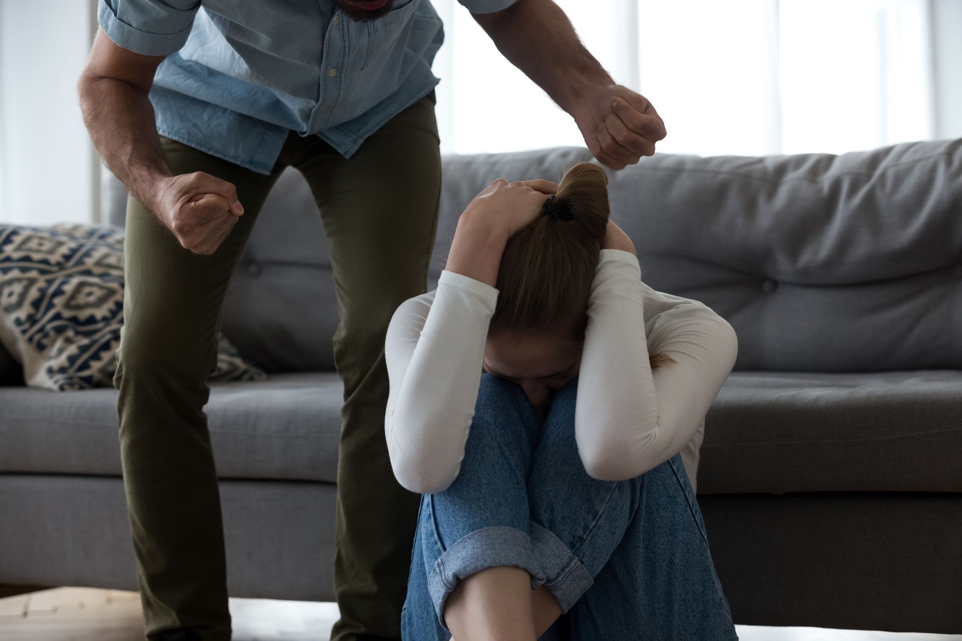 Person crouches beside a crying child seated on the floor in a living room, comforting them.