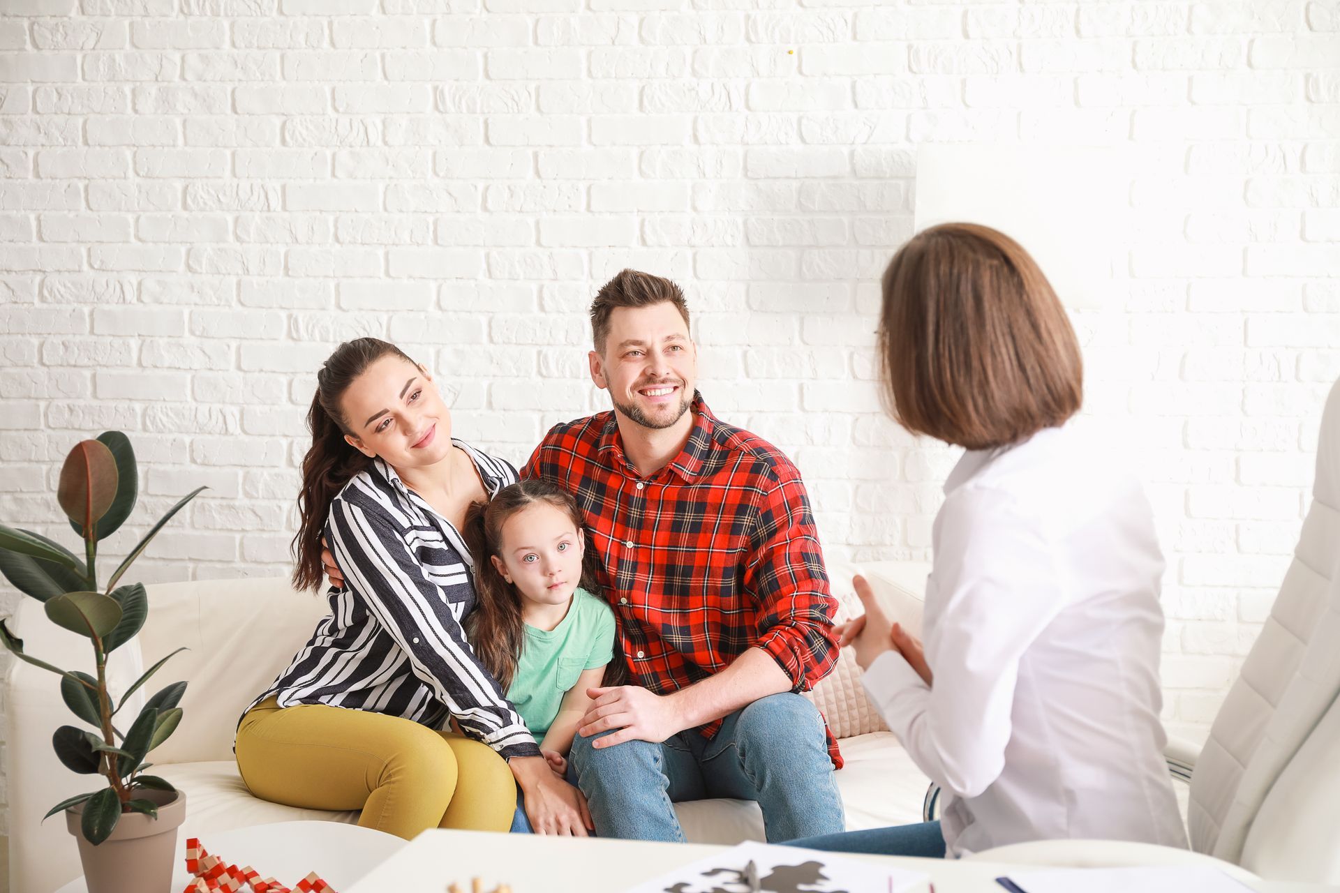 Family talking with a counselor in a bright living room, seated on a sofa with a child between parents.