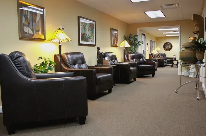 Comfortable waiting room with black leather chairs, warm lighting, and beige carpet.
