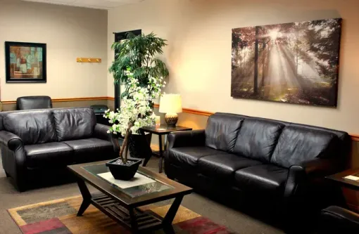 Modern living room with black leather sofas, coffee table, lamp, and wall art