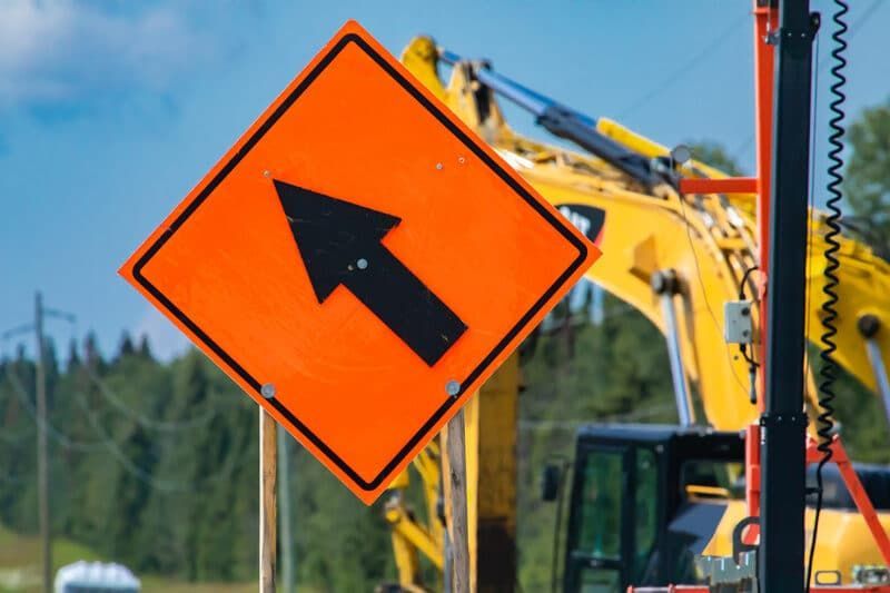Orange roadwork sign with black arrow in front of construction equipment