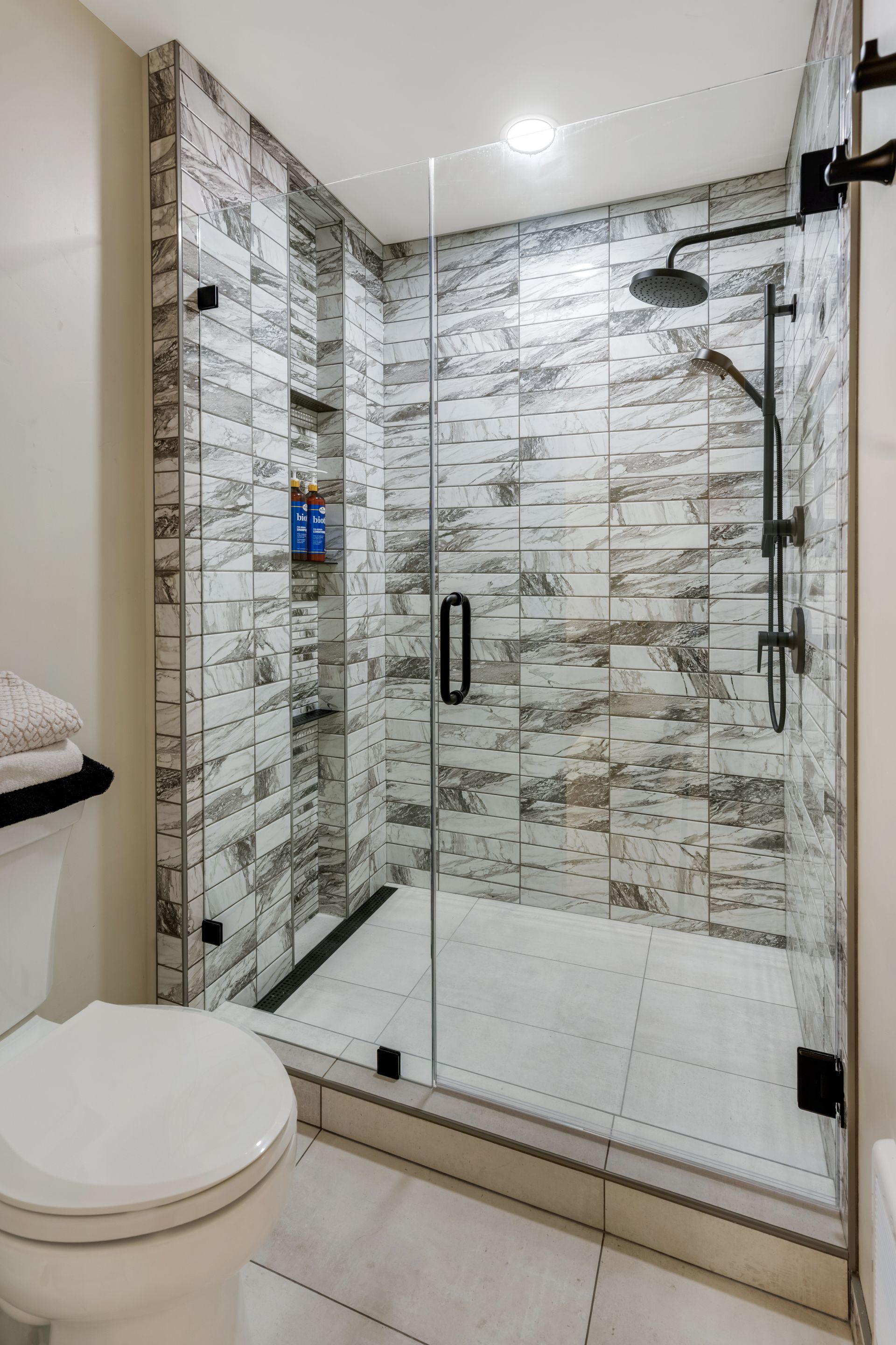 Modern tiled bathroom with glass shower enclosure and toilet in the foreground