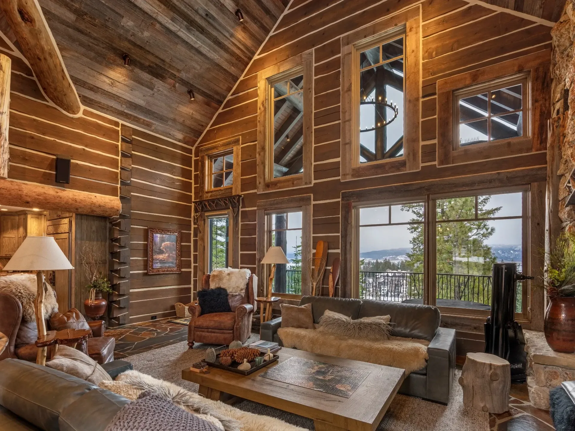 Rustic log cabin living room with large windows, stone fireplace, and mountain view