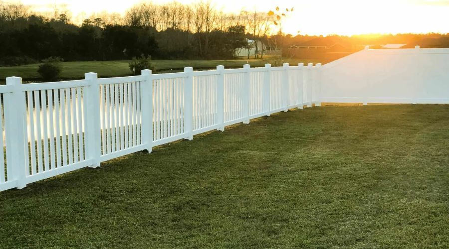 White vinyl fence installation surrounding a backyard lawn at sunset.