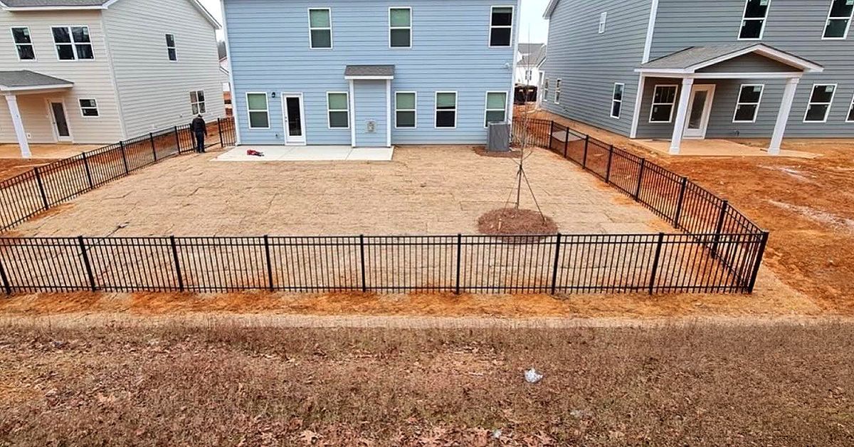 Black metal fence enclosing a front yard with mulch, between two light-blue townhouses