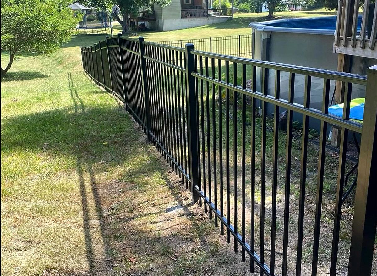 Black metal fence along a grassy yard beside a backyard pool and deck in sunlight