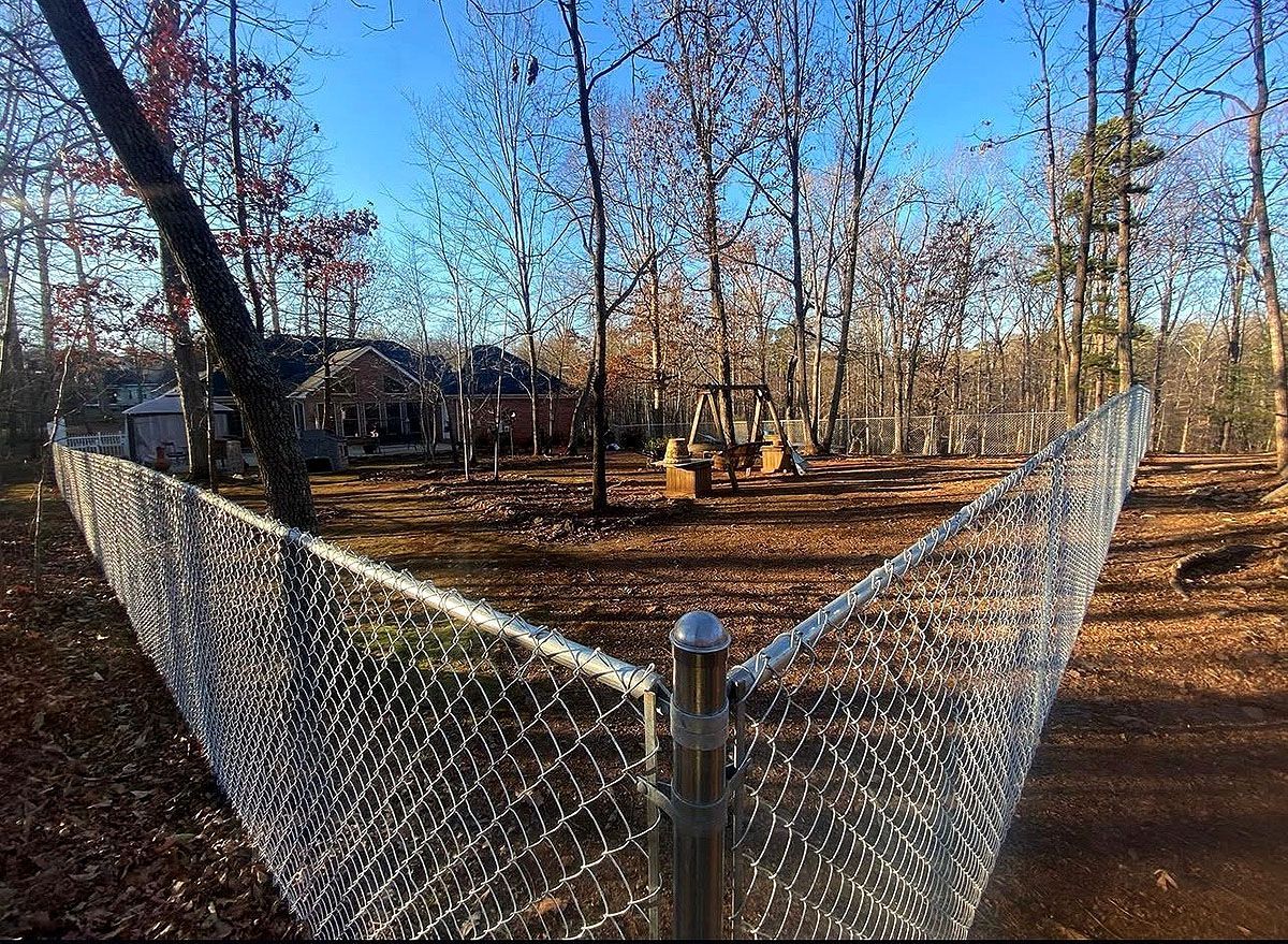 Chain-link fence around a wooded yard with a house and playground in the background