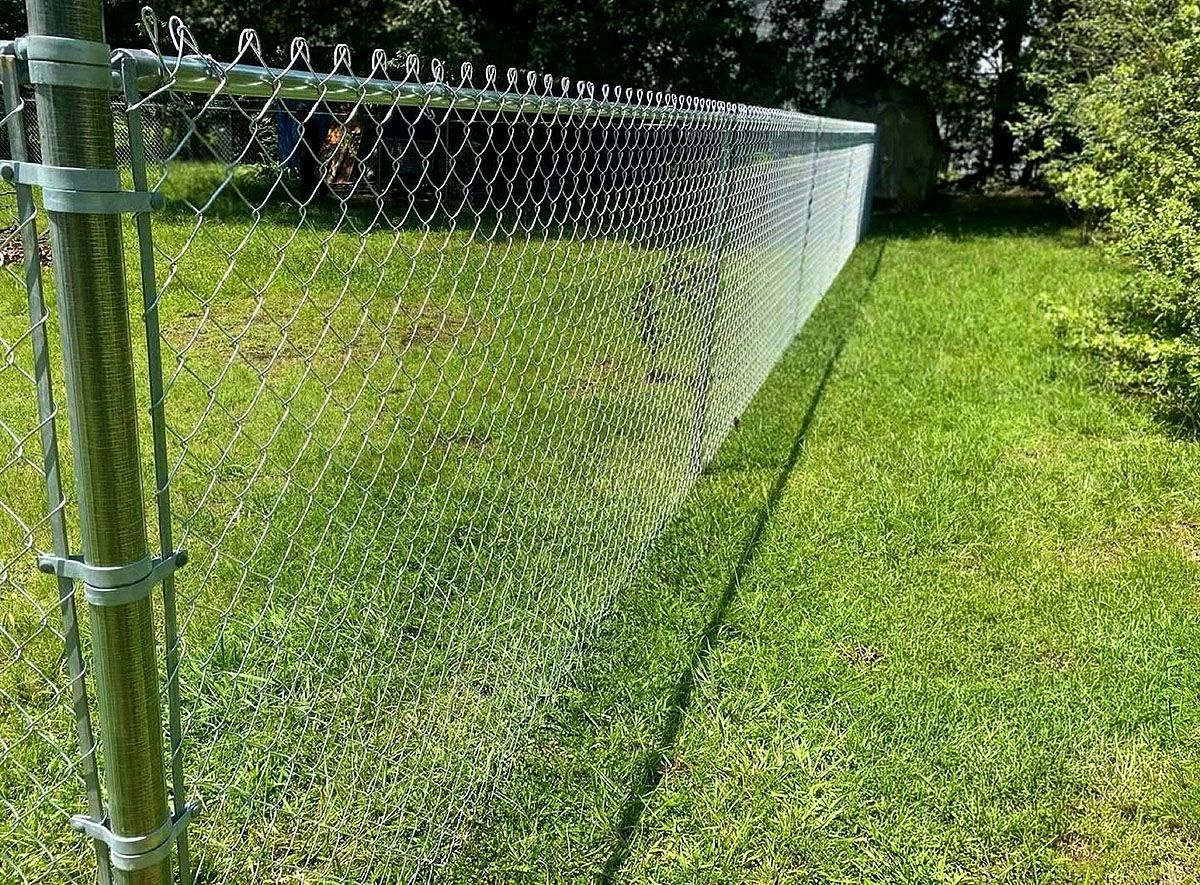 Chain-link fence along a grassy yard, casting a diagonal shadow in sunlight.