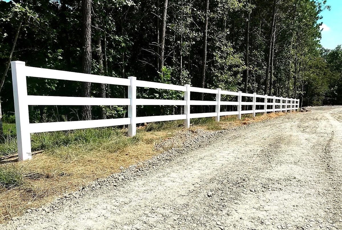 White wooden fence along a gravel road beside a wooded area