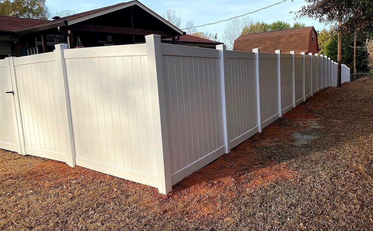 White vinyl privacy fence enclosing a yard beside a house on a leaf-covered slope.