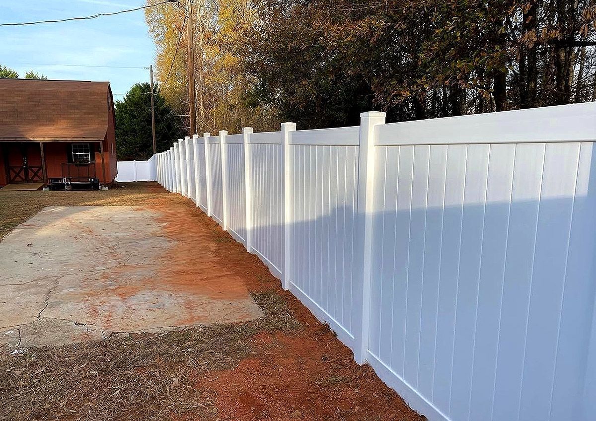 White vinyl fence along a gravel driveway beside a brick house and autumn trees